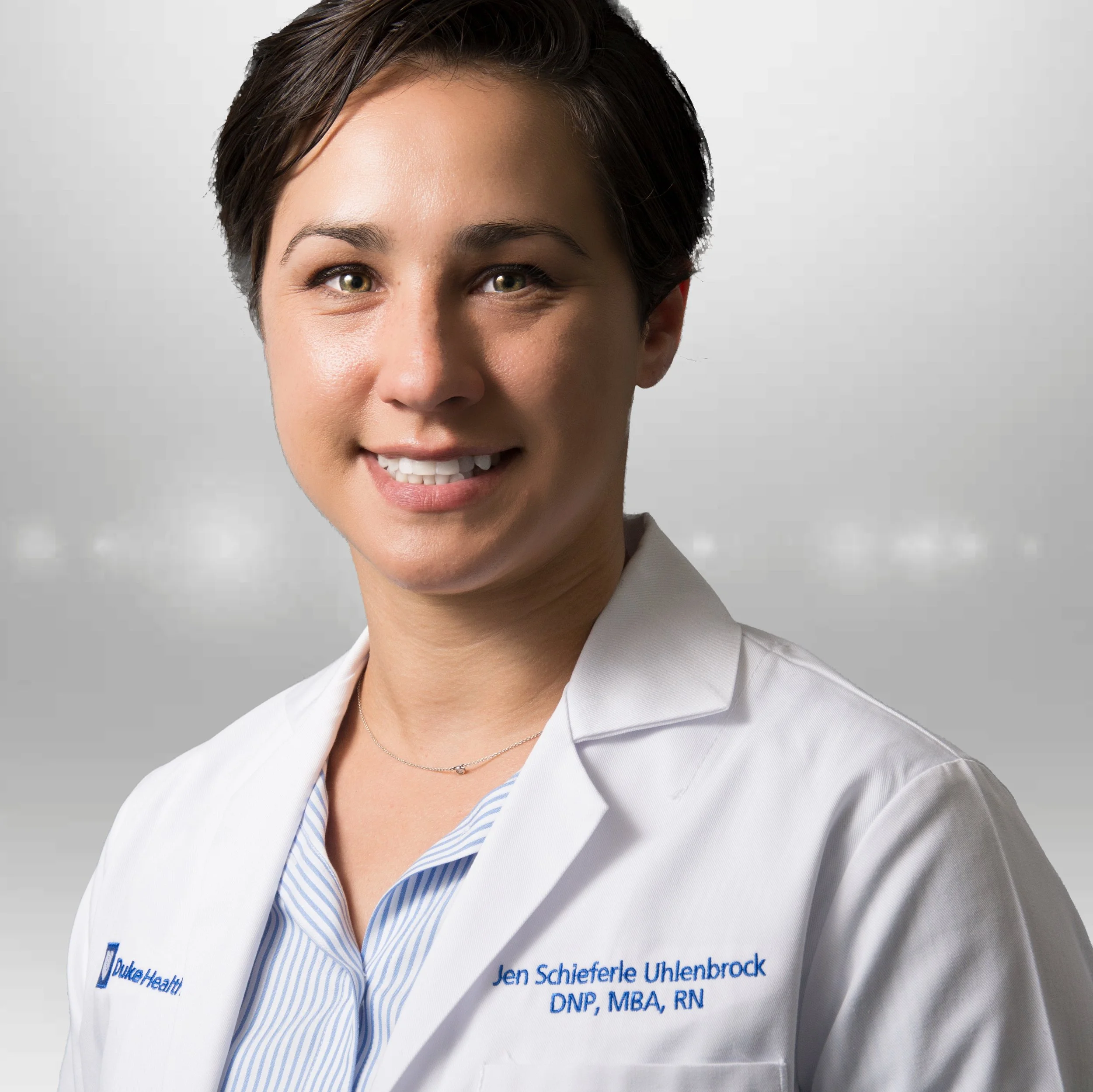 Professional headshot of Jen in a white coat against a gray background