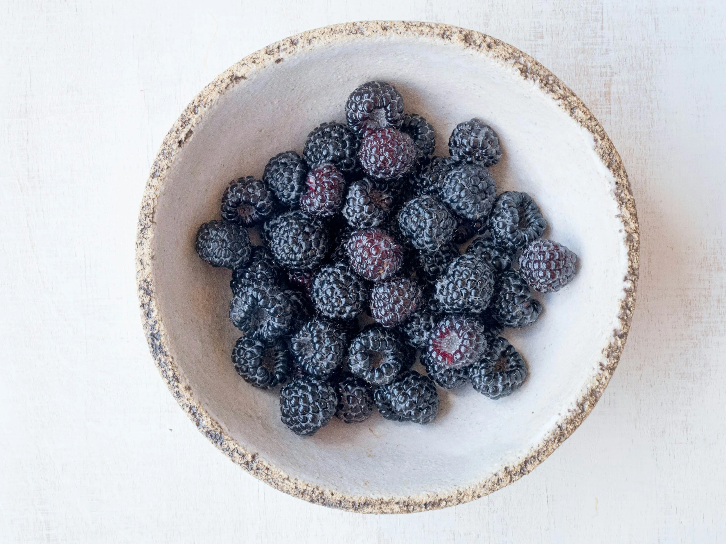 A white ceramic bowl filled with blackberries on a white surface.