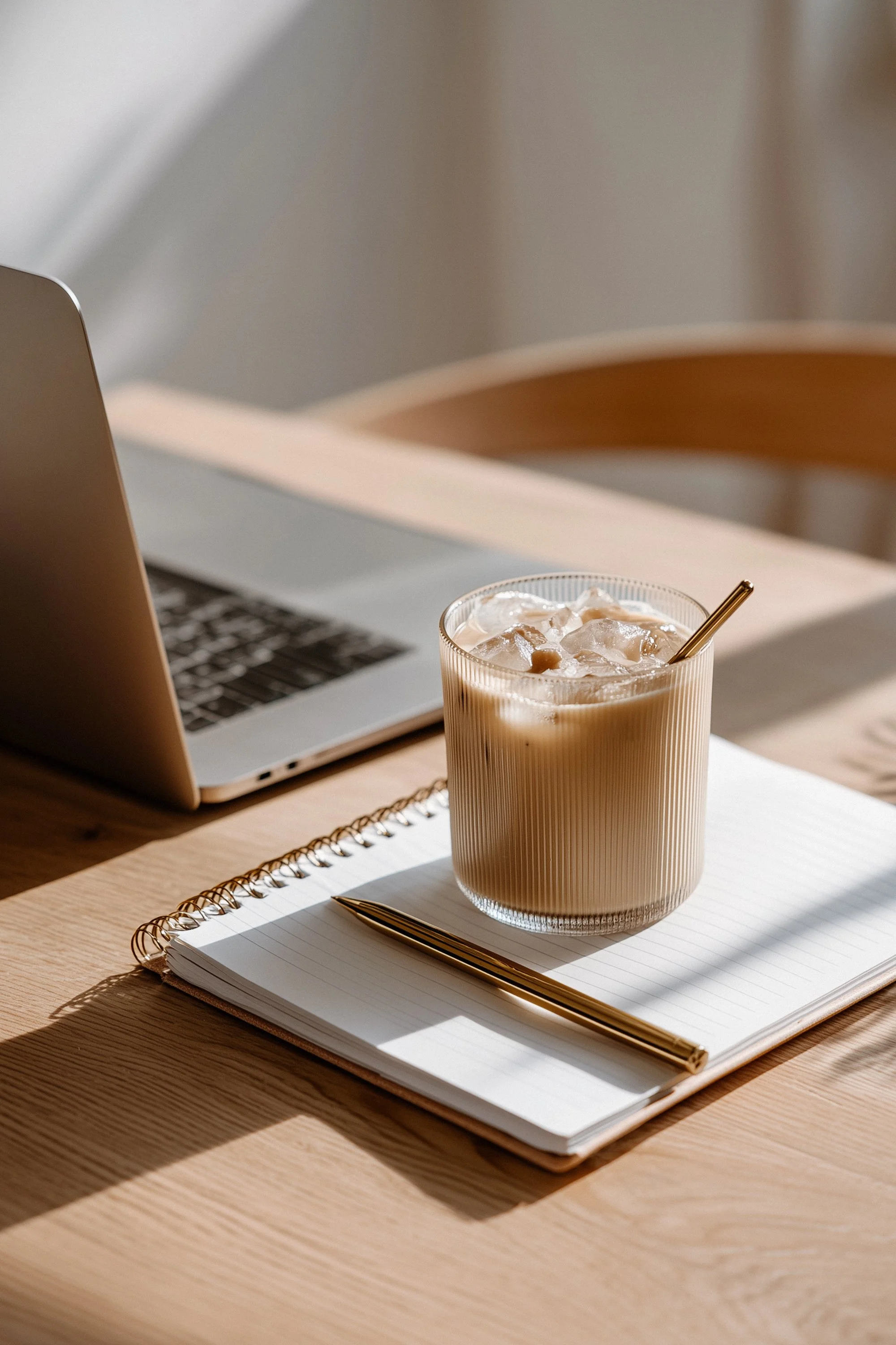 image of an iced coffee, notepad, pen and laptop on a desk