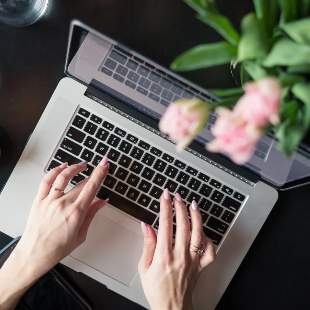 a blogger on a computer with pink flowers out of foucus in the foreground