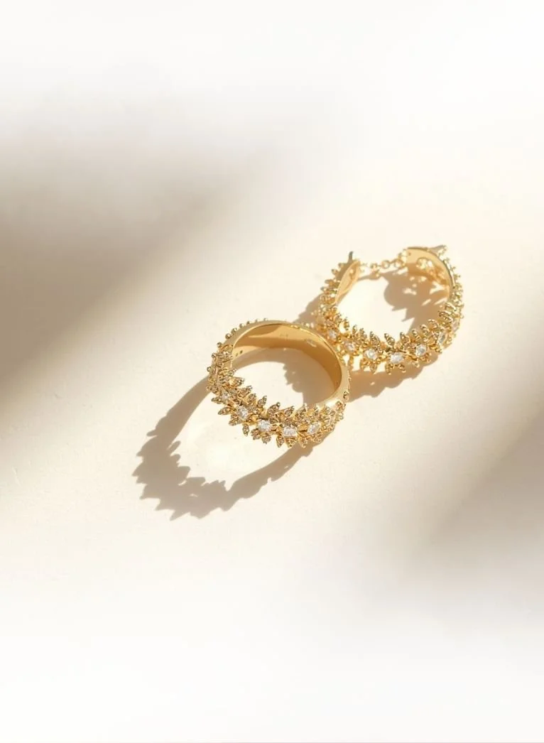 gold and diamond earrings sparkling in the sunlight on a neutral background