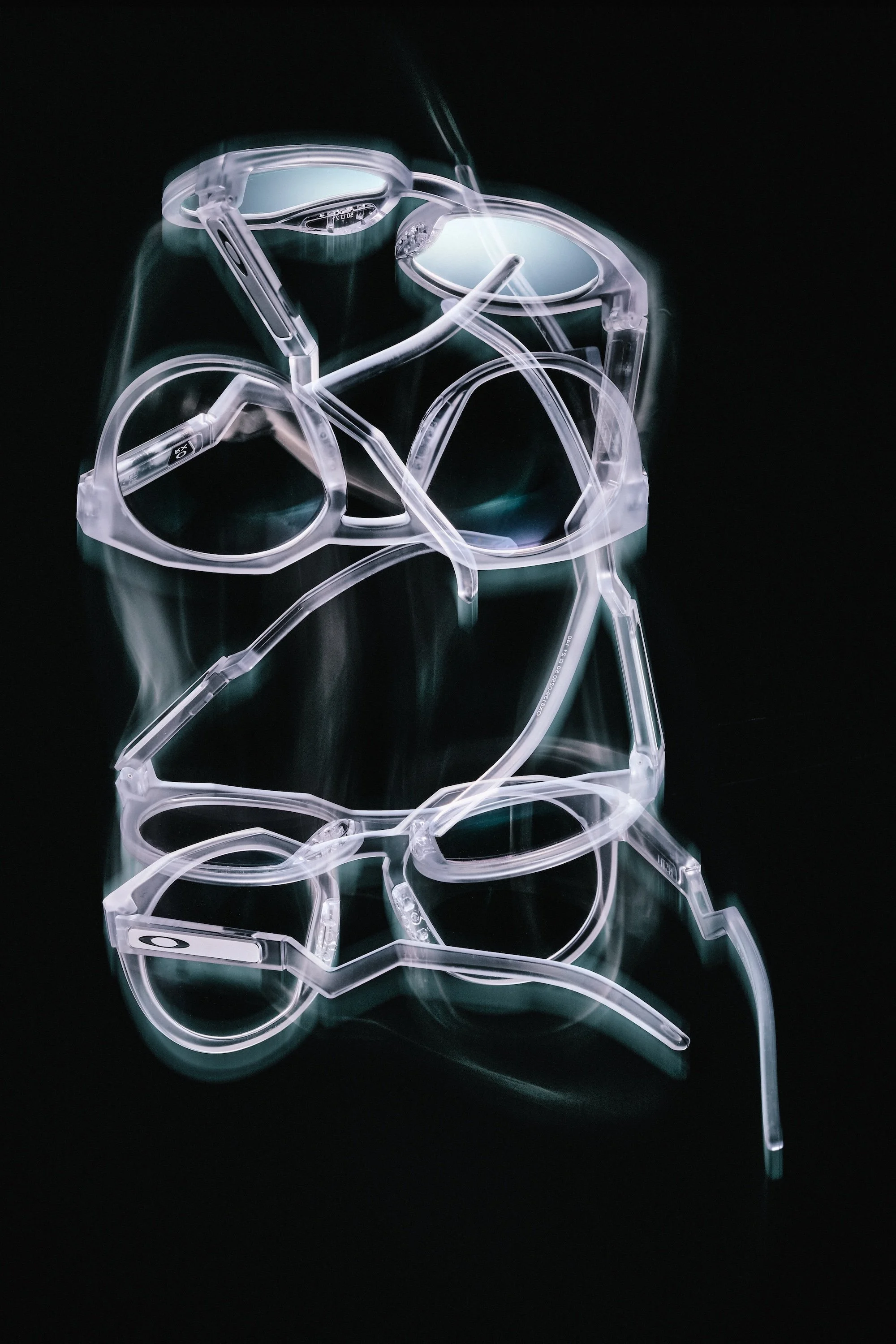 A collection of transparent Oakley HSTN eyeglasses arranged on a dark reflective surface, creating a mirror image.