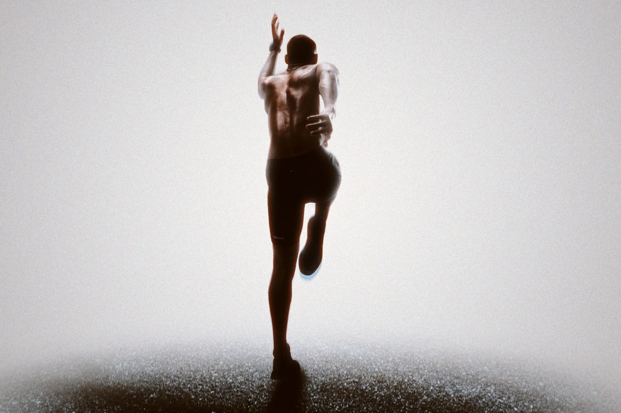 A person running on a track with a trail of water spray behind them, silhouetted against a bright sky.