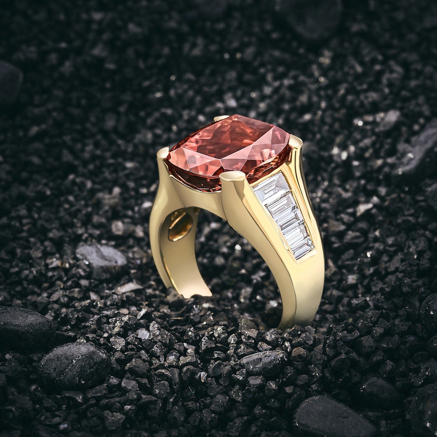 Gold ring with large red gemstone and baguette diamonds on black textured surface.