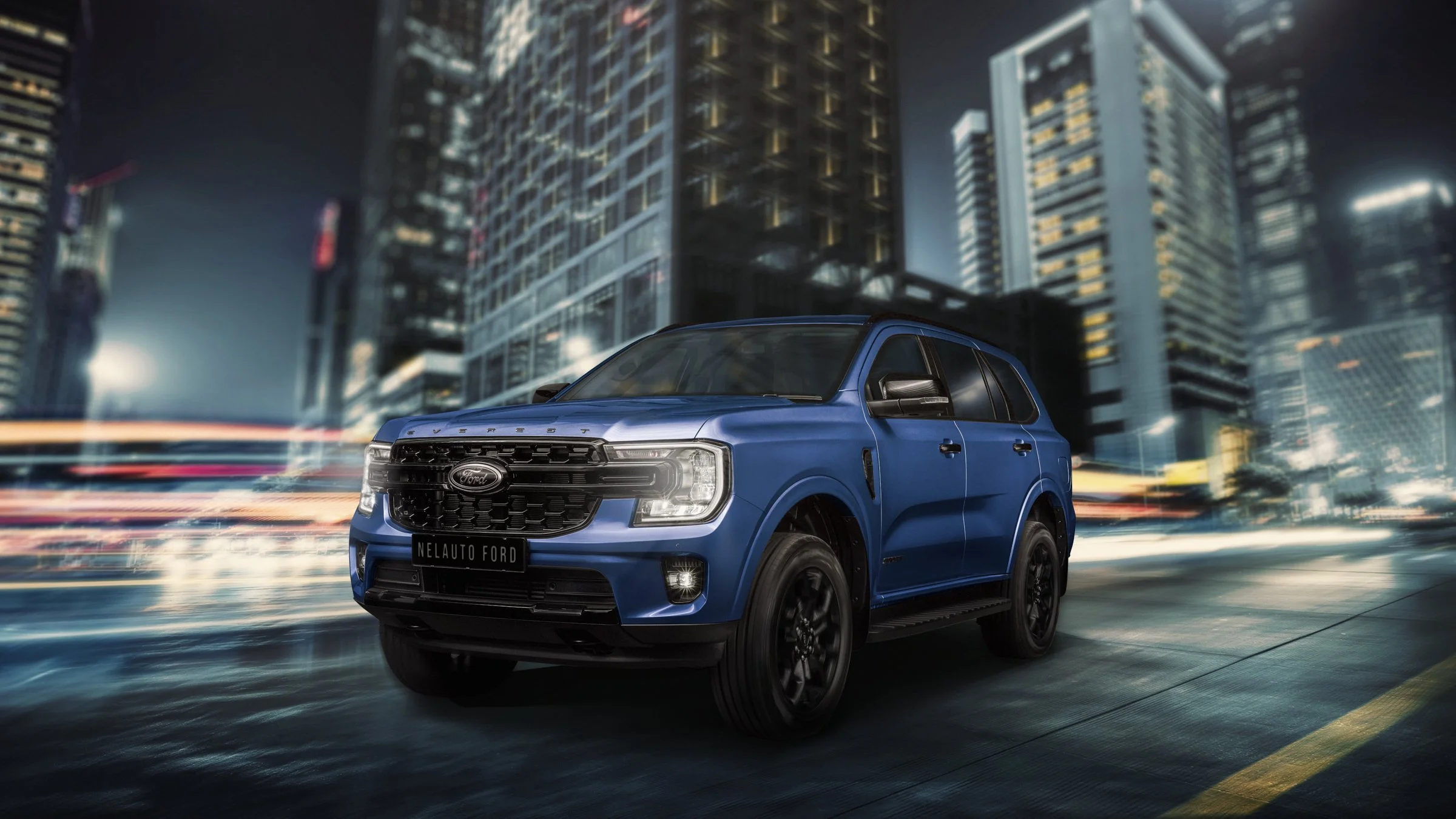 A blue Ford Everest SUV is driving on a city street at night with tall buildings and light trails in the background.