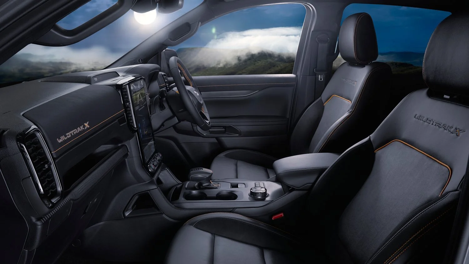 Interior of a Ford Wildtrak-X vehicle with leather seats, dashboard, and steering wheel, view through open car window towards landscape with mountains and clouds.