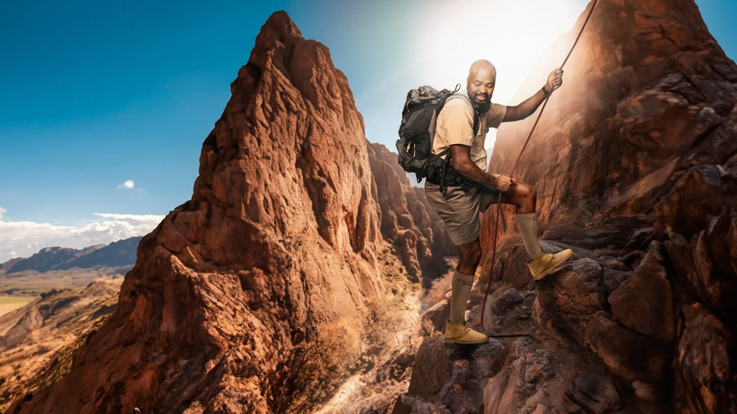 Man rock climbing on a rocky terrain with a clear blue sky.