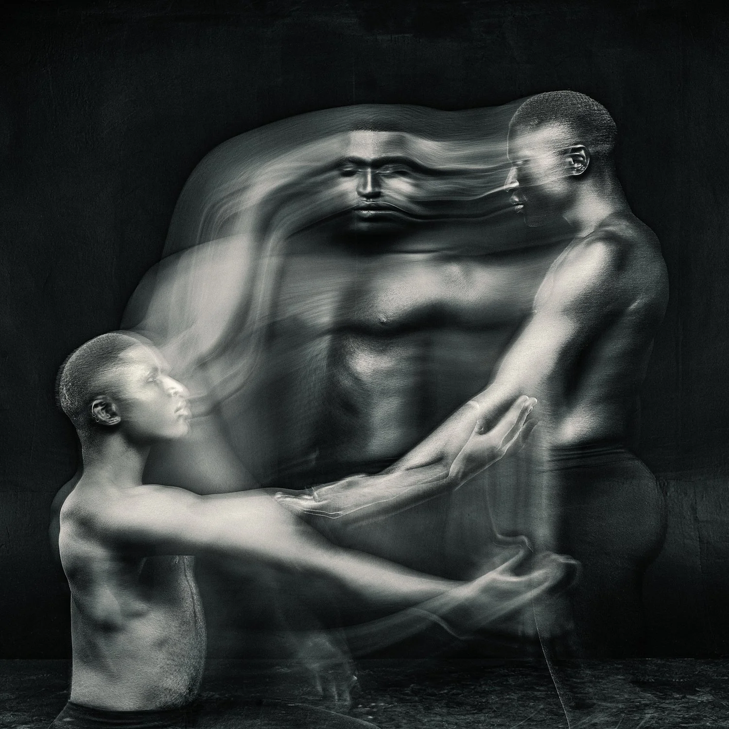 Artistic photo of blurred male figures in dynamic poses, suggesting motion and fluidity, on a dark background.