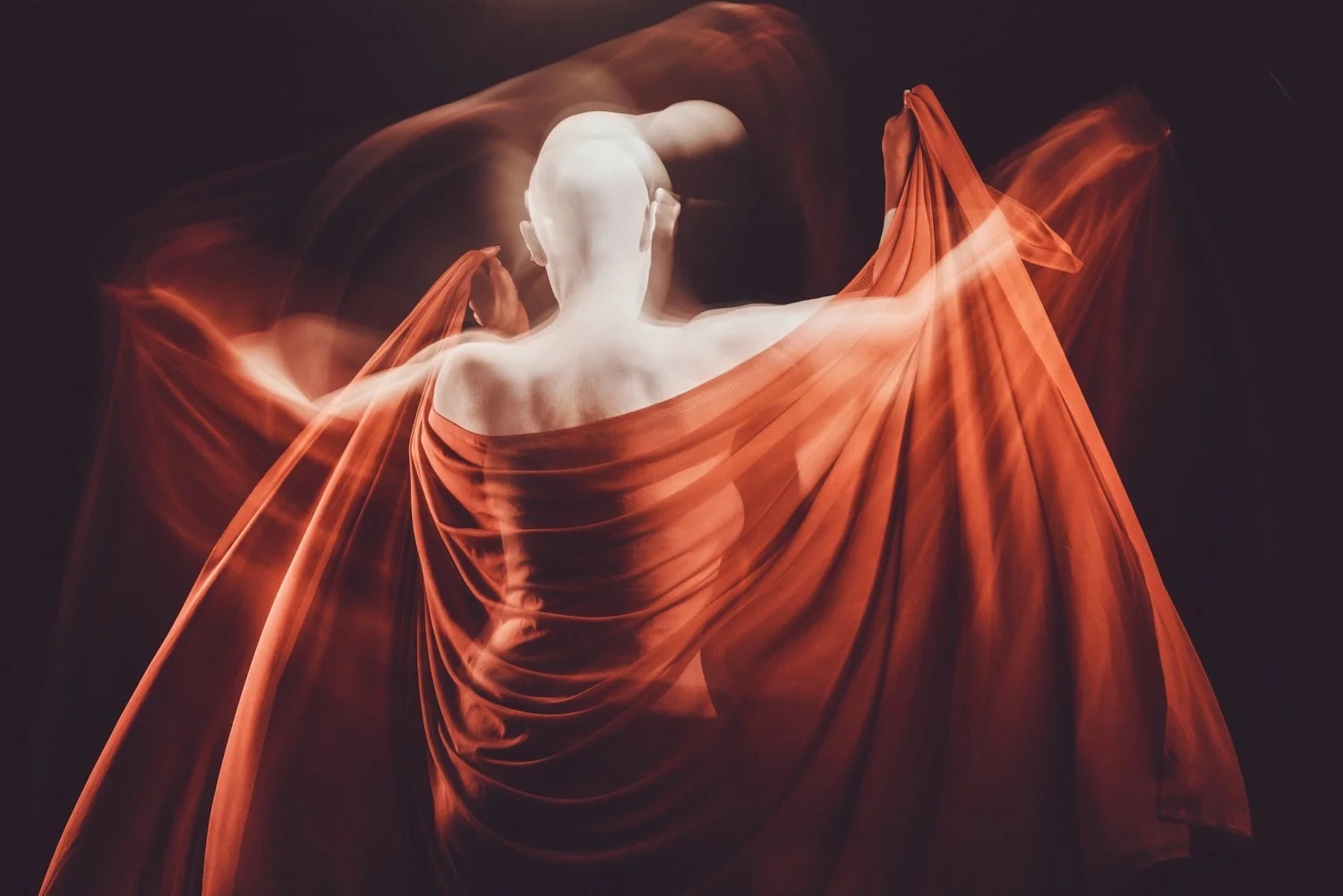 Bald person wrapped in flowing red fabric with blurred motion effect.