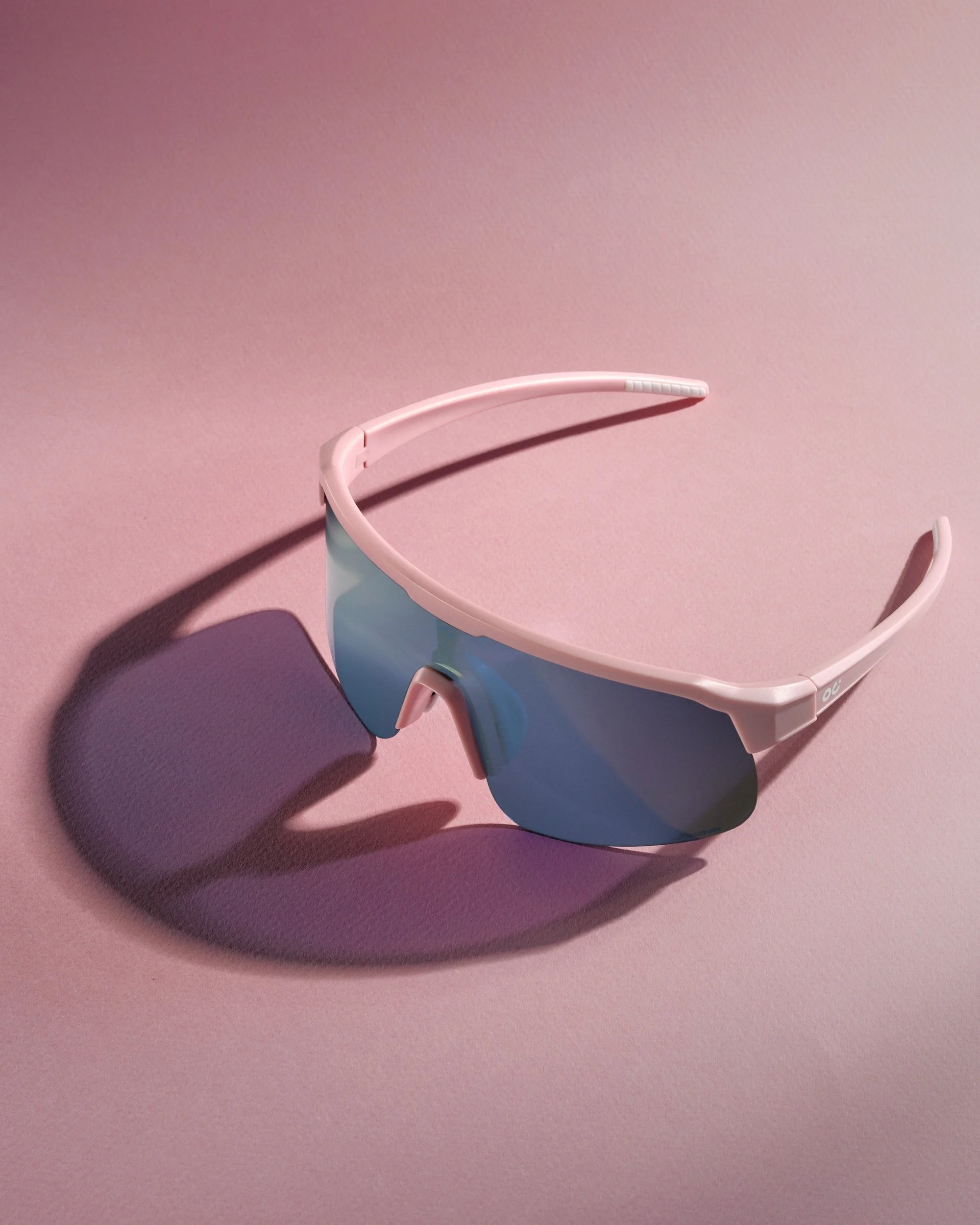 Pink and blue sunglasses cast a shadow on a pink surface.