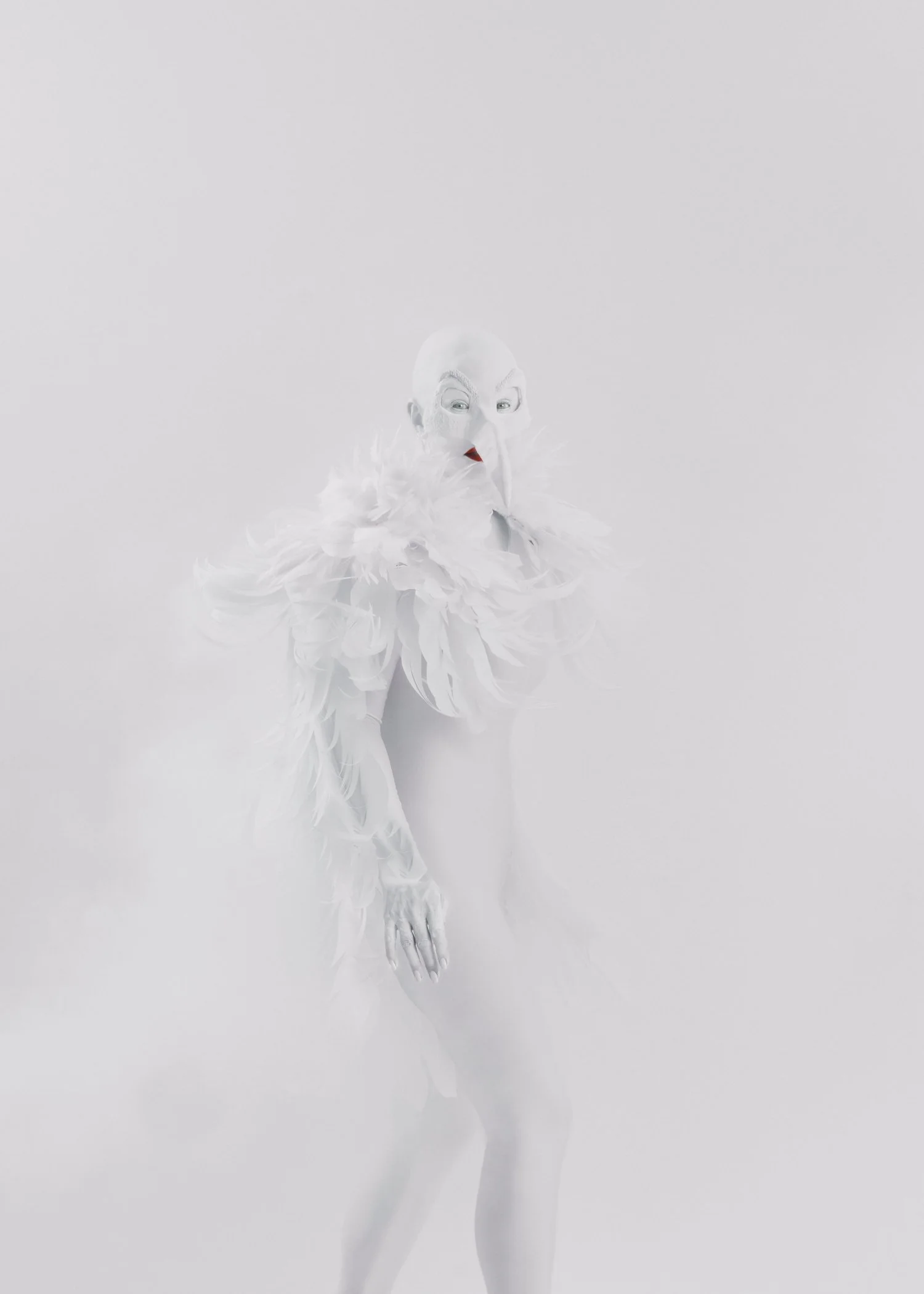 Person in a white, feathered costume with a bird-like beak mask, standing against a plain background.