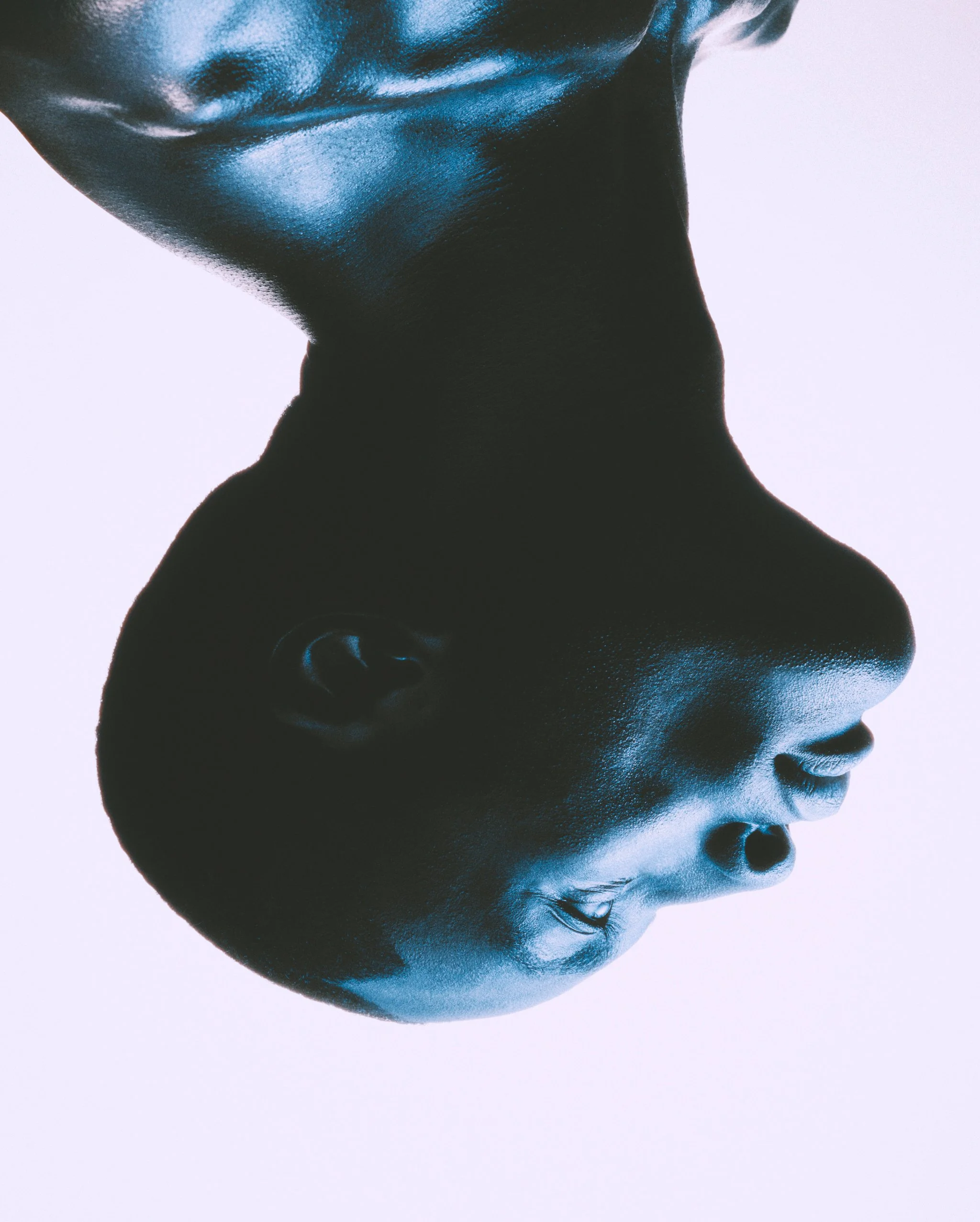 Close-up upside-down profile of a man's face with smooth skin, aquamarine lighting highlighting facial features, and a high-contrast background.