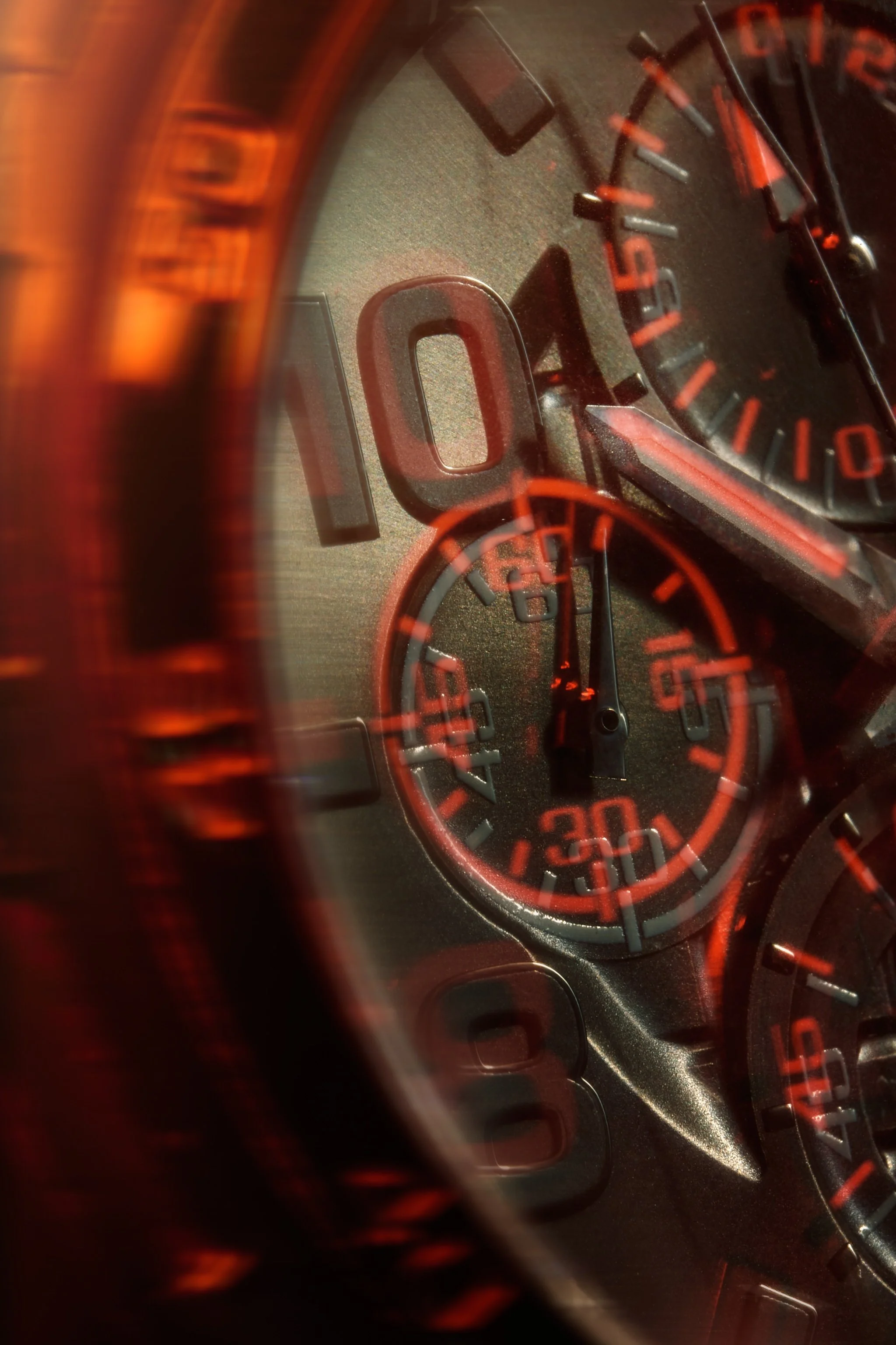Close-up of a watch face showing the tachometer, and other gauges through a red-tinted reflection.