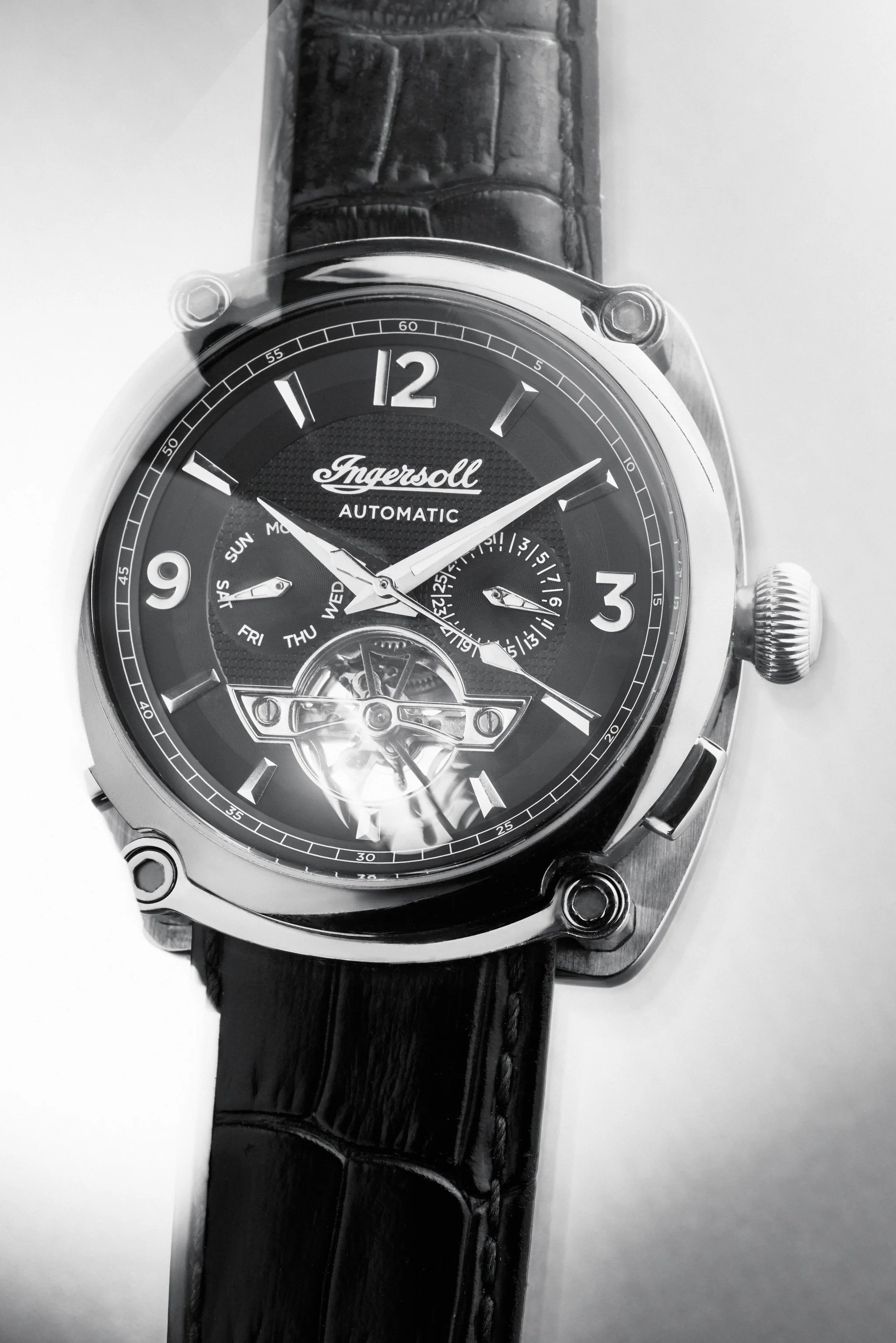 A black and white photograph of a wristwatch with a black leather strap, a round face, and multiple subdials. The watch brand is Ingersoll, and it shows the time as approximately 10:10