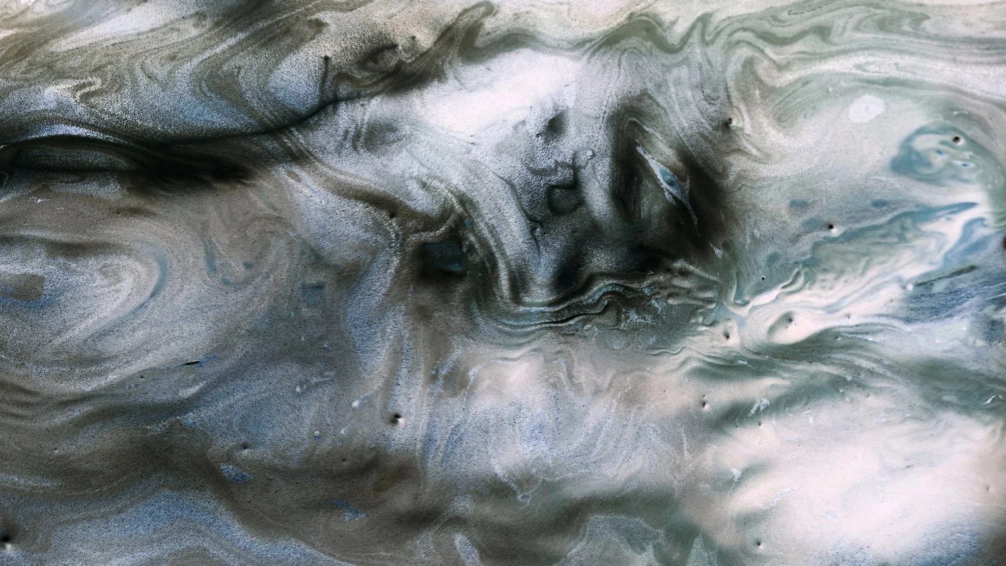 Abstract swirling mixture of black, white, gray, and hints of blue colors in a fluid pattern.