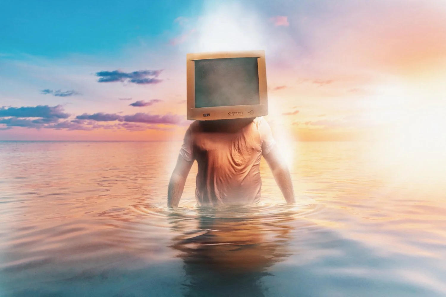 Person standing in water with a computer monitor for a head at sunset.