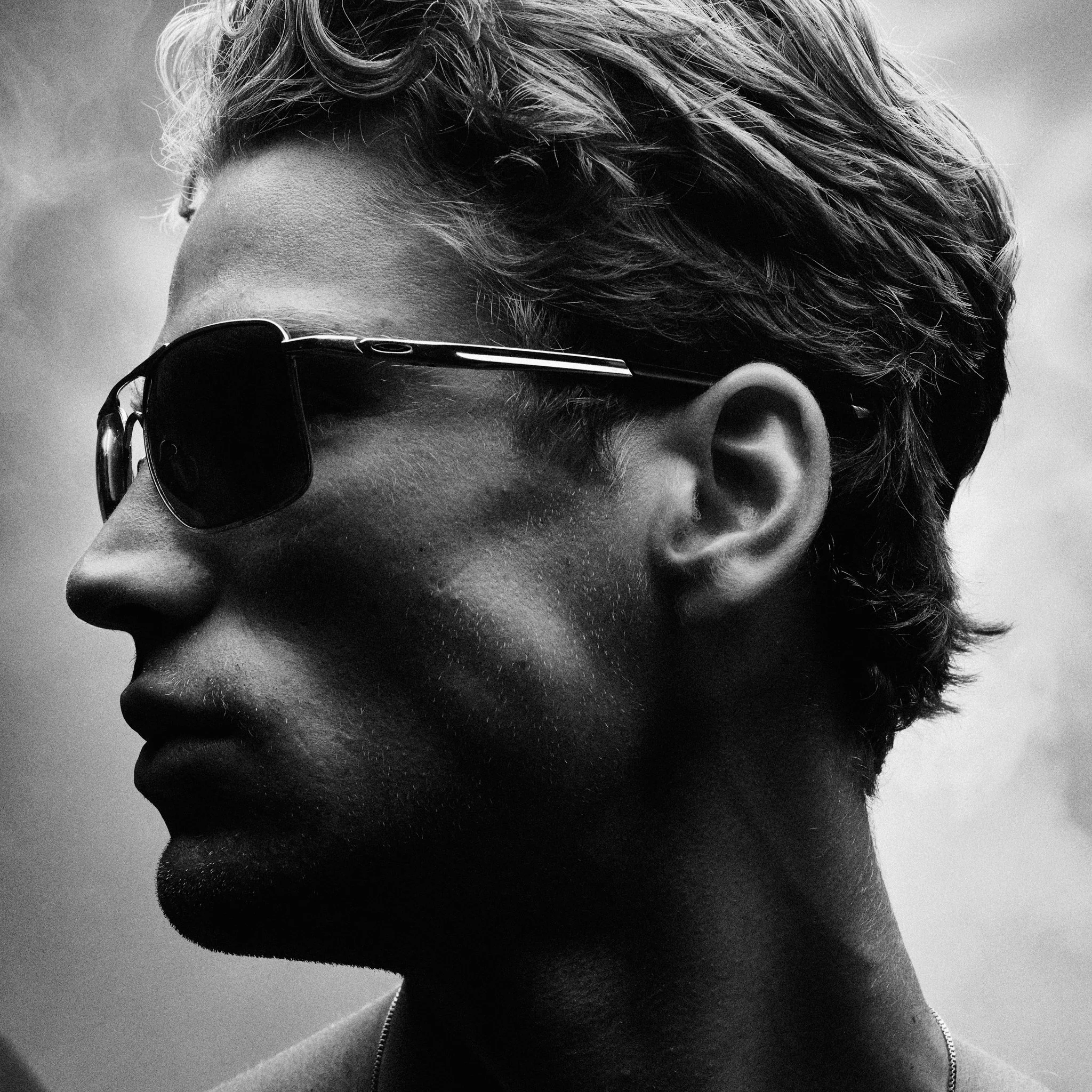 Black and white side profile of a person wearing sunglasses, with short hair and a defined jawline.