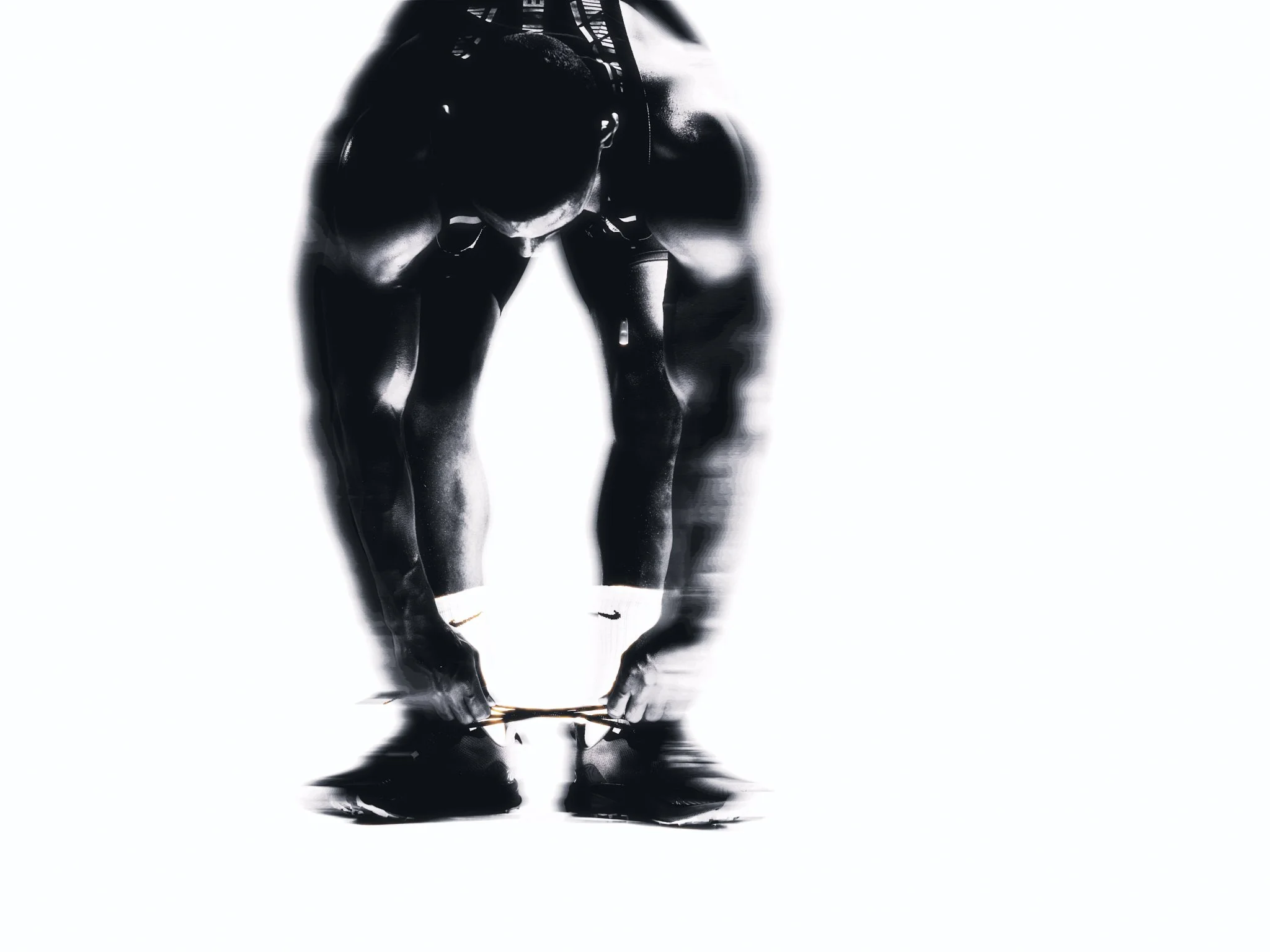 A black and white image of a runner standing, bending forward, with their head down and tying their shoes, seen with motion that creates a rippled effect.