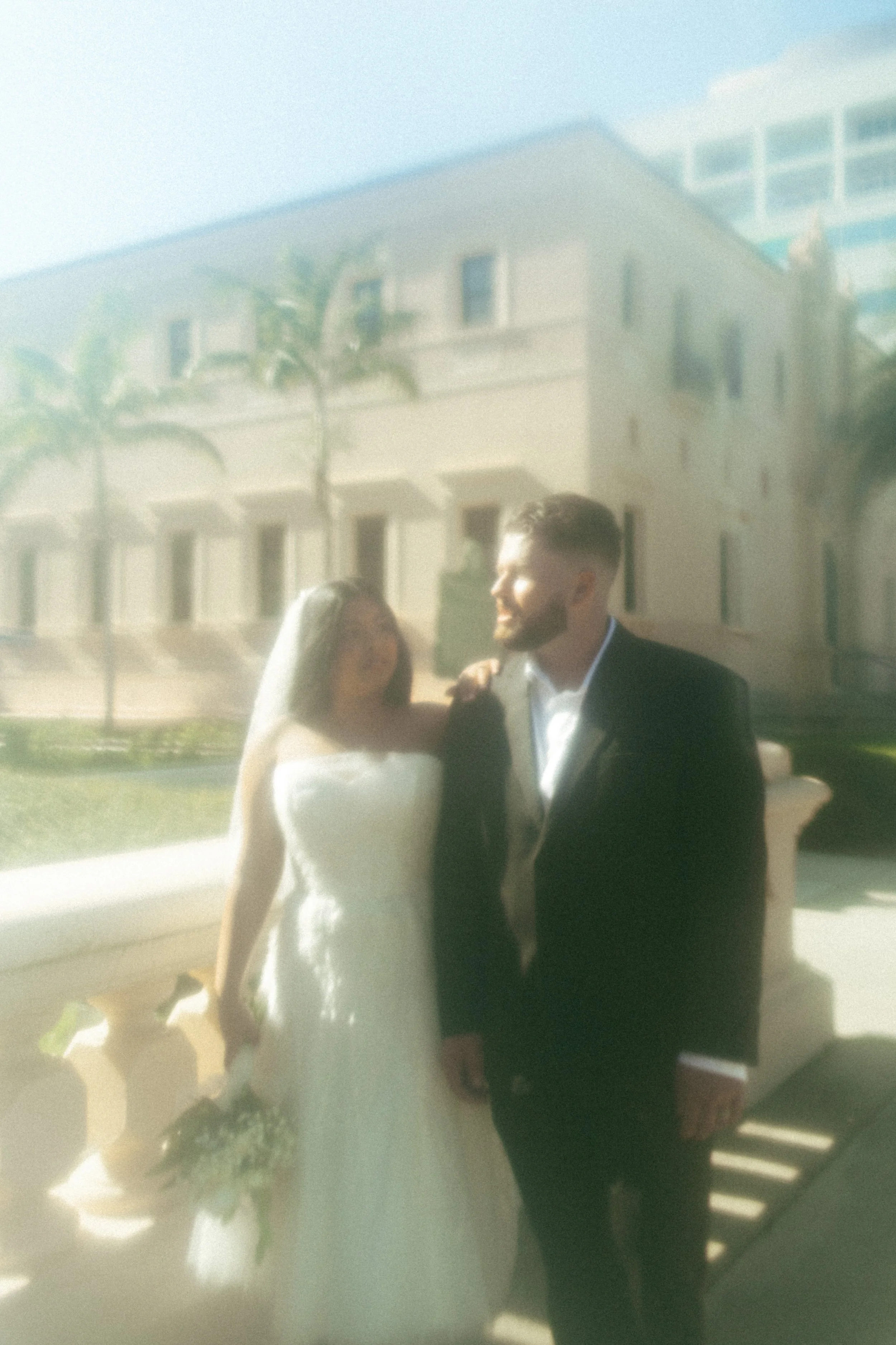 A bride and groom standing together outdoors during a bright, sunny day.