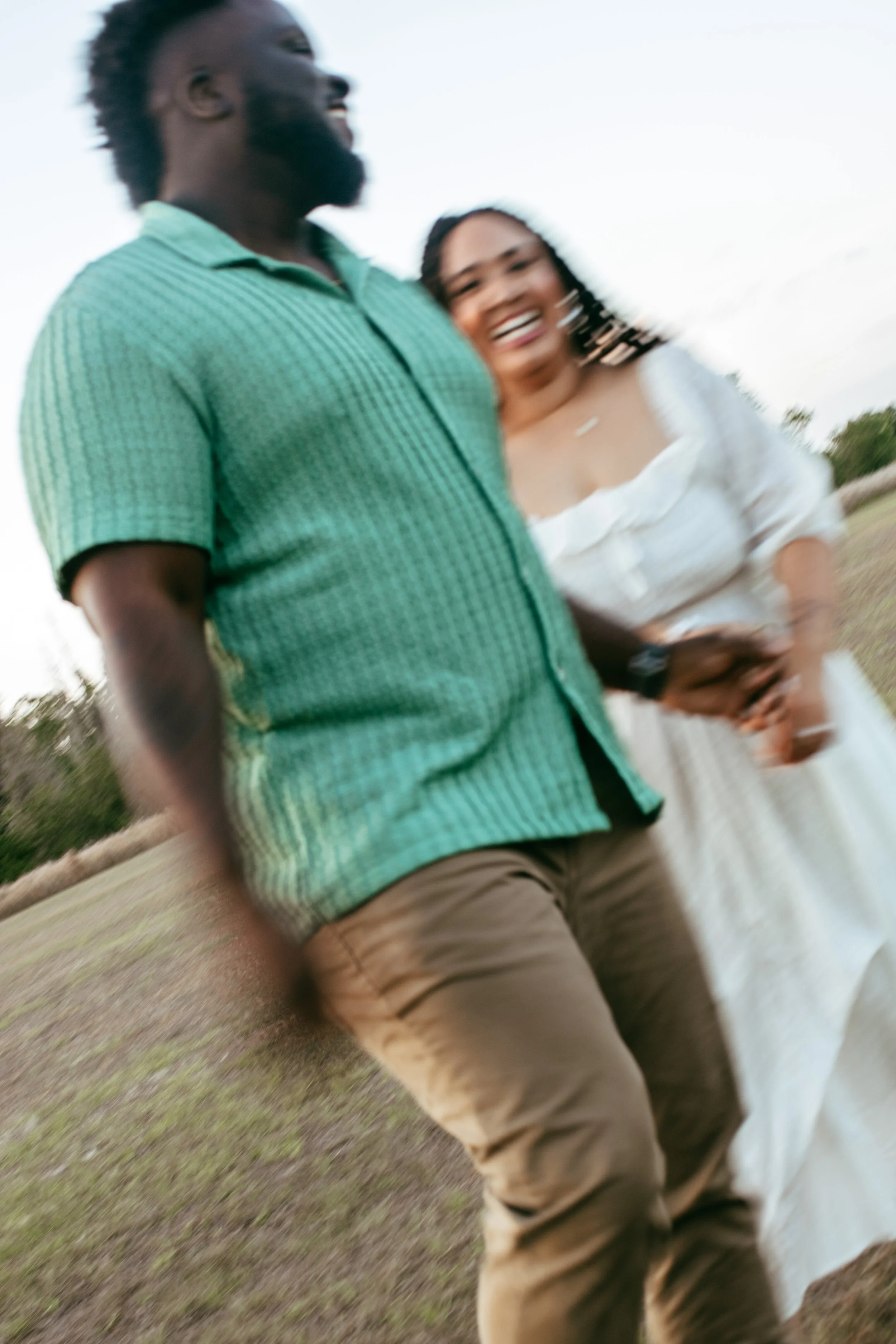 A man and woman standing outdoors, holding hands, smiling and enjoying each other's company, in a natural setting.