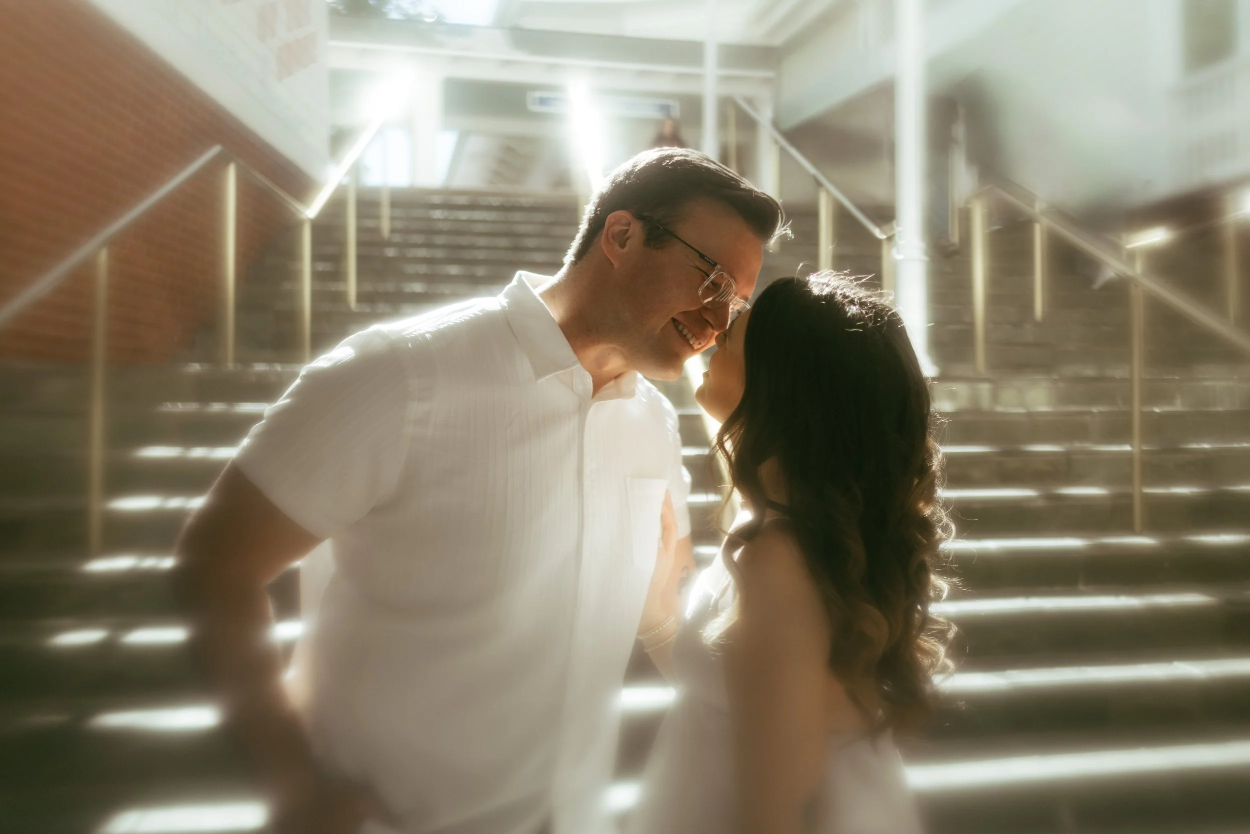 A couple sharing a close, intimate moment on a stairway, with light shining behind them.