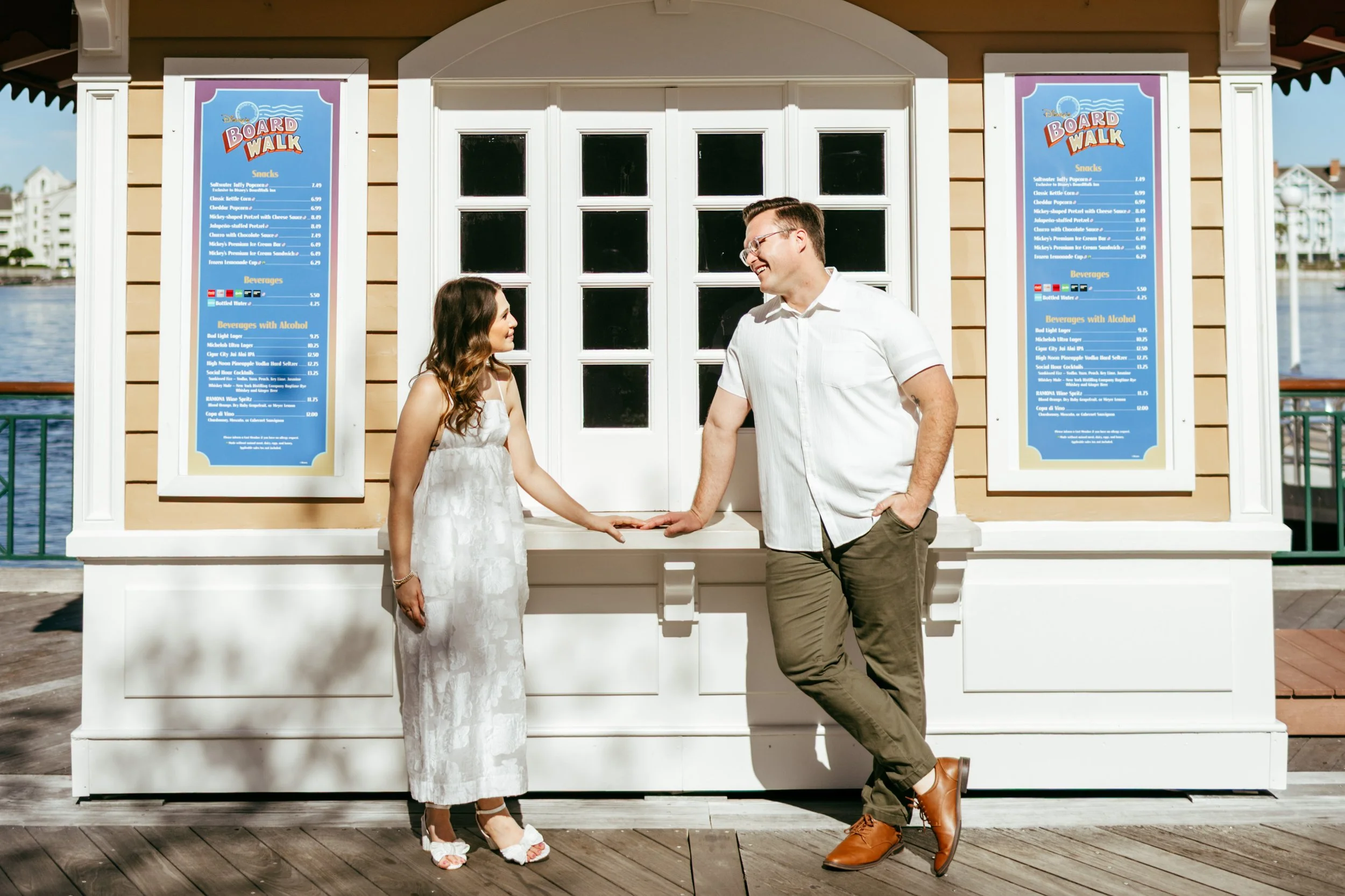 A young woman and a young man standing outside a small building with menus posted on the walls, holding hands and smiling at each other.