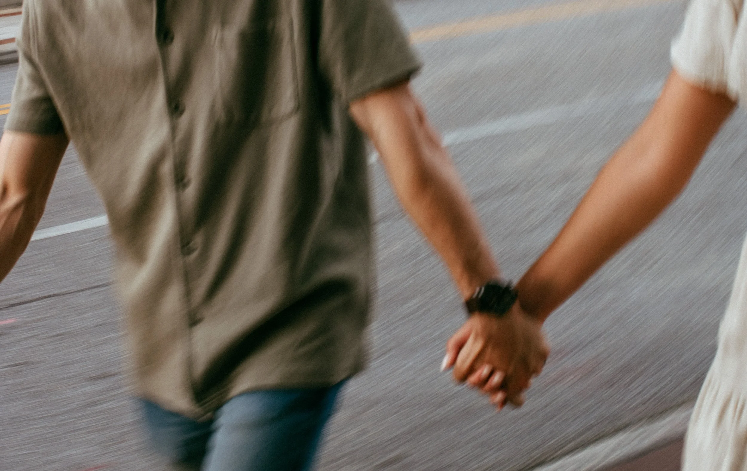 Two people holding hands while walking on a road.
