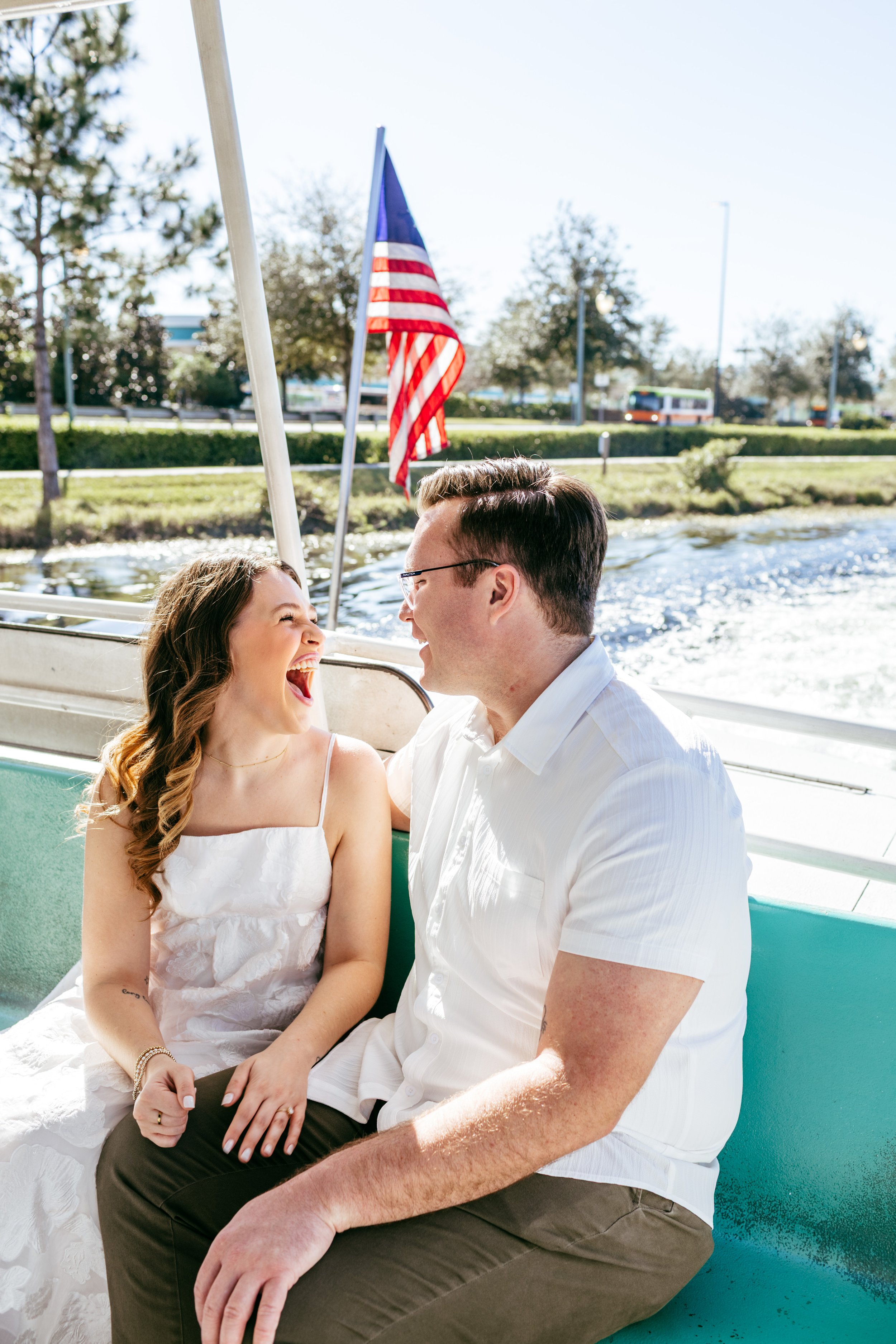 A couple smiling and laughing while sitting on a boat with American flags in the background.