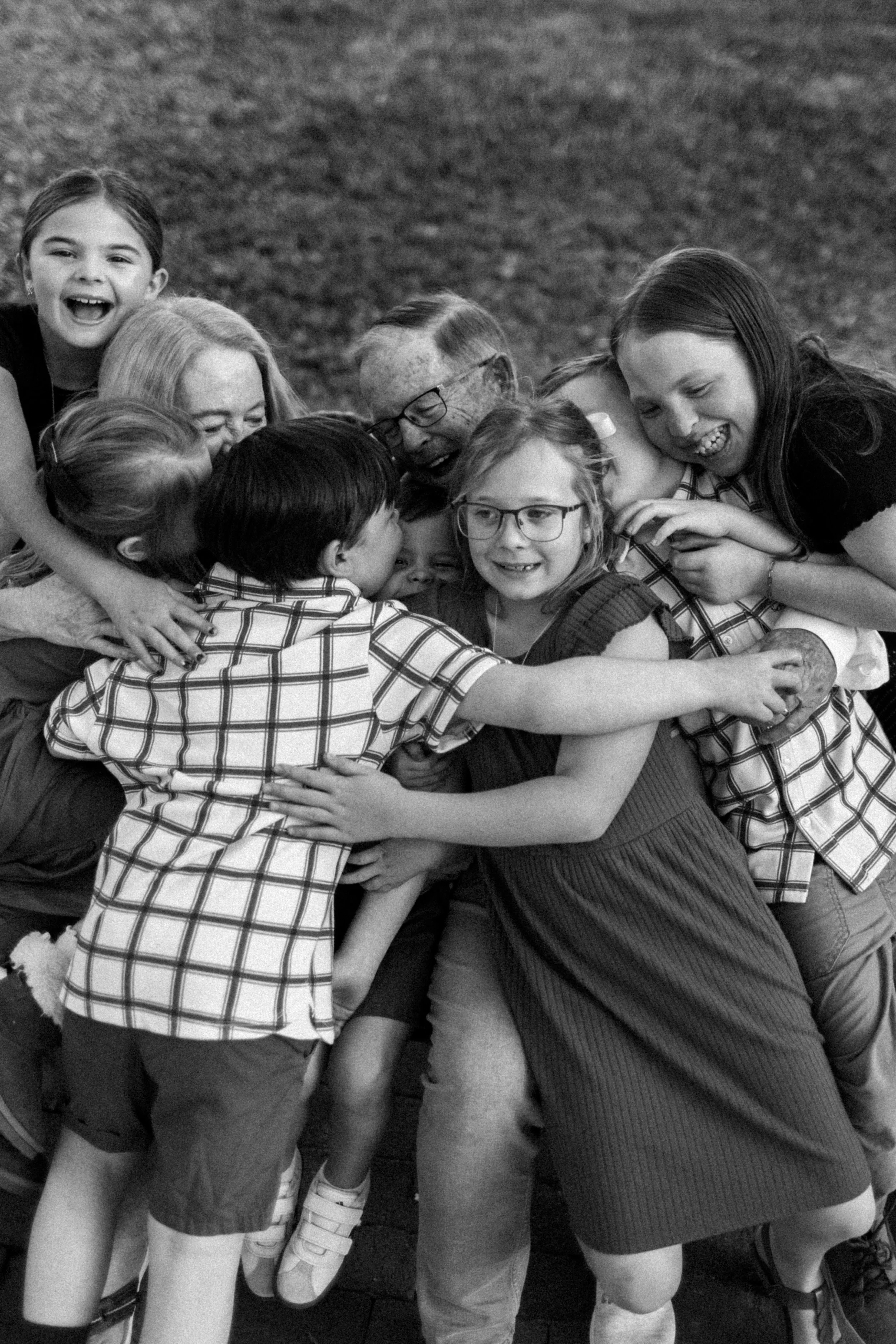 Group of children and adults embracing and playing together outdoors, laughing and smiling.