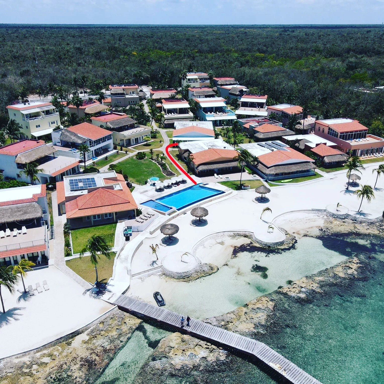 Aerial shot of Costa del Sol beachfront resort in Cozumel โ features include a swimming pool, colorful vacation homes, sandy beach, palm trees, and oceanfront lounge areas.
