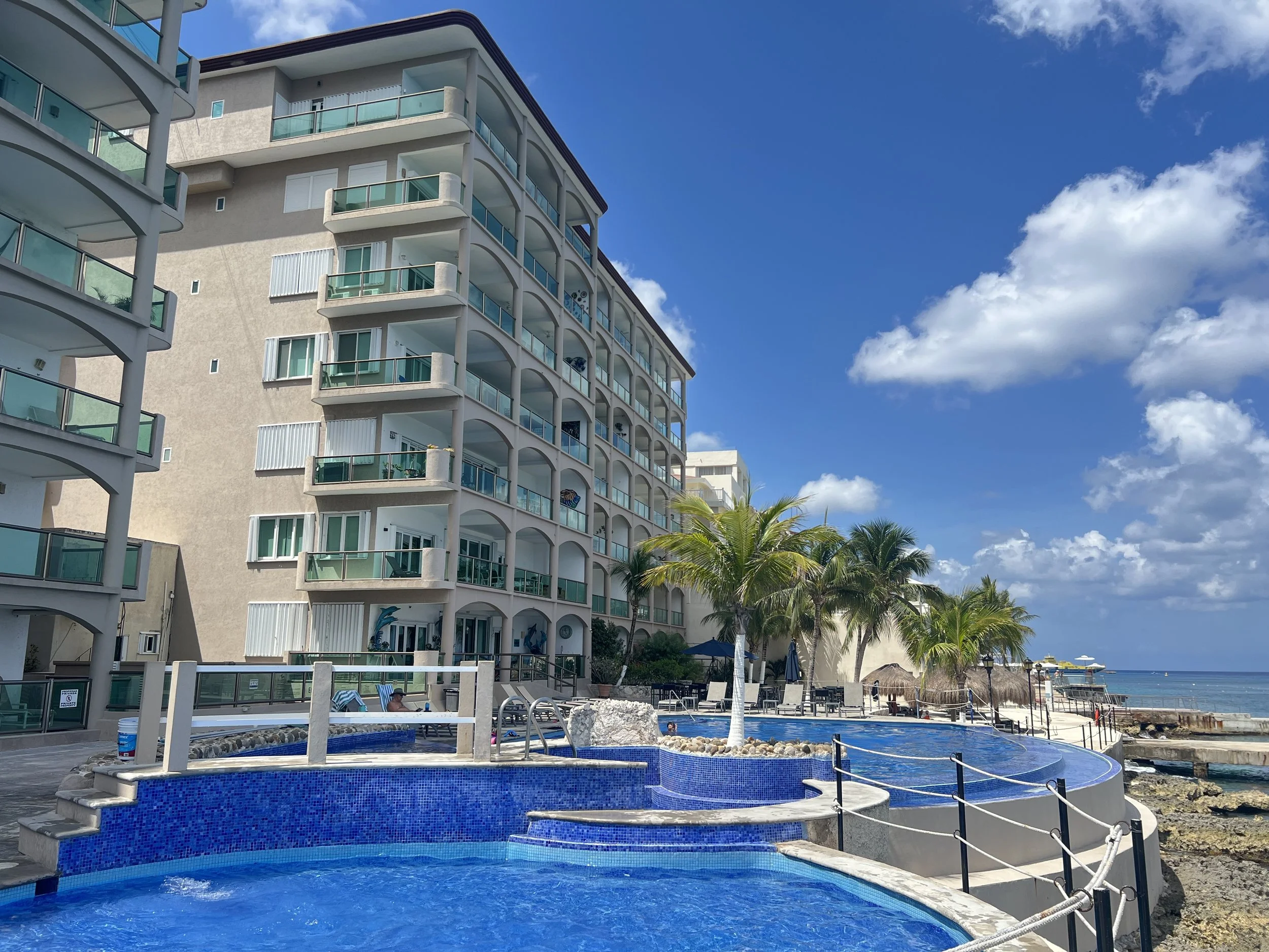 El Cantil oceanfront condominiums in Cozumel viewed from the Caribbean Sea, with waterfront pool, palm trees and private pier.