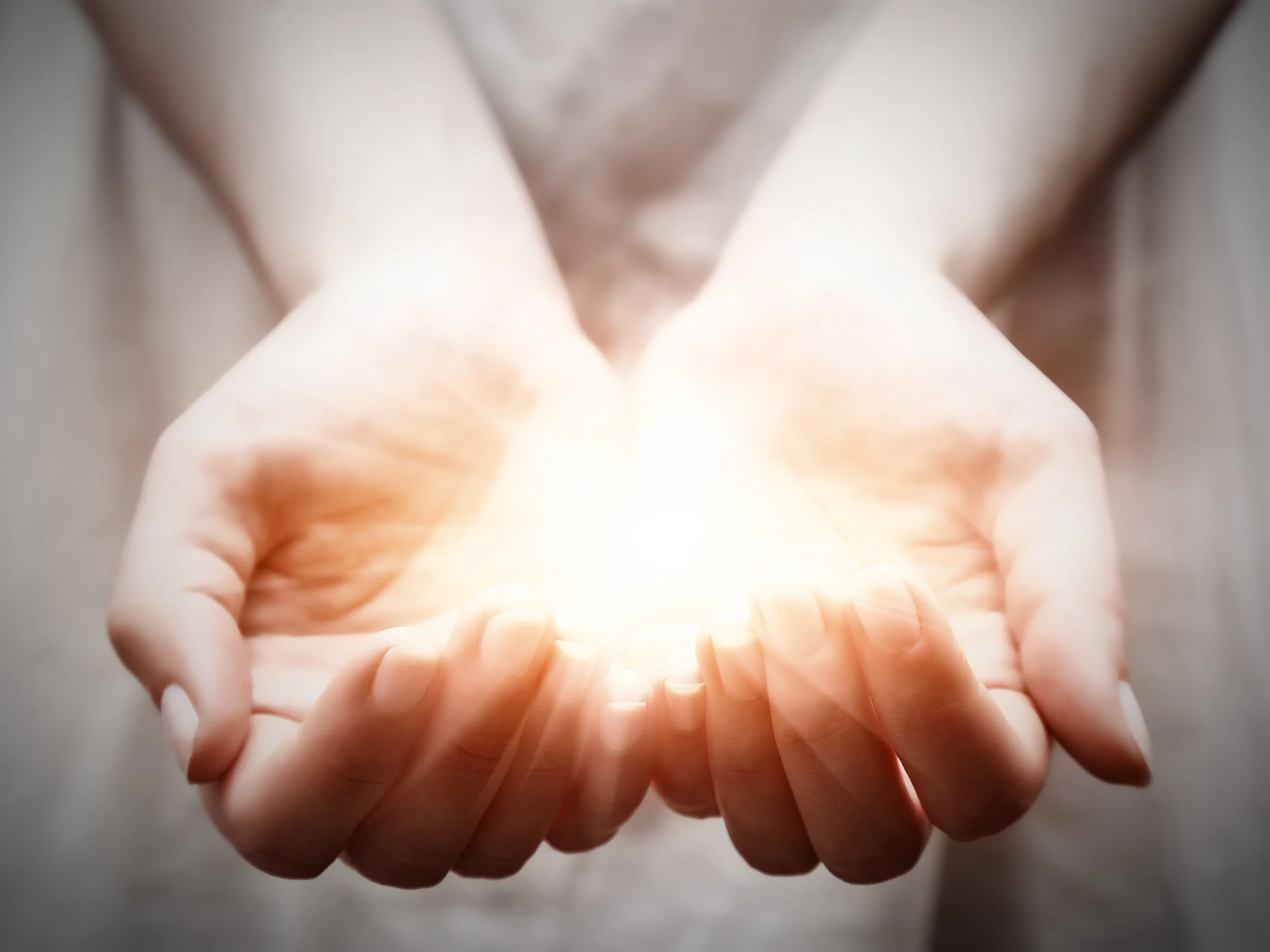 Open hands holding a glowing light, symbolizing energy or hope.