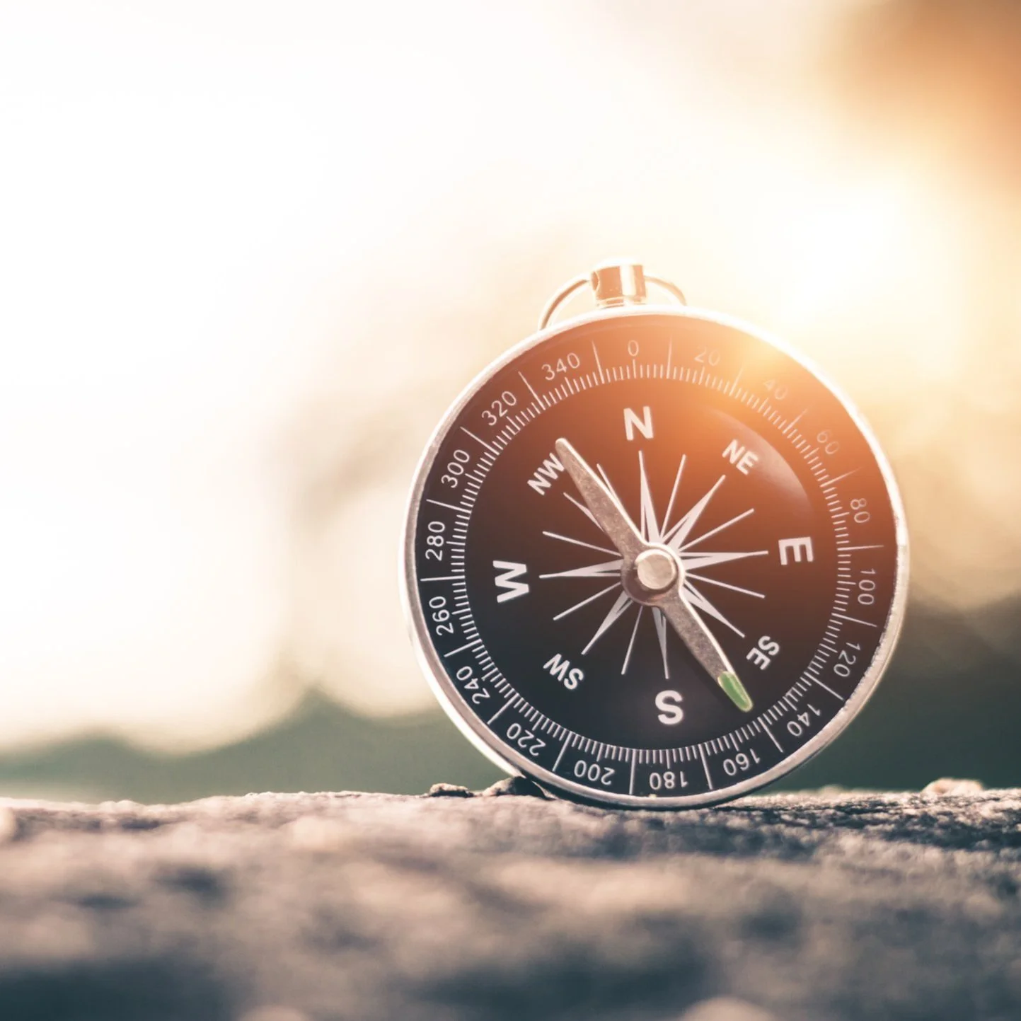Close-up of a black compass on a rock with sunlight in the background.