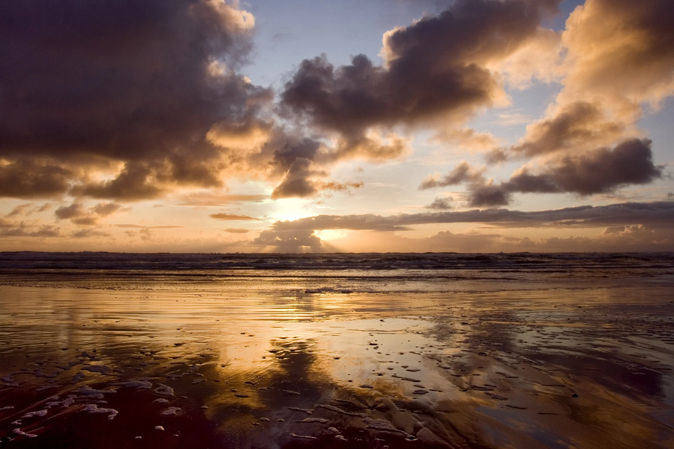 Sunset over ocean with clouds and beach reflections