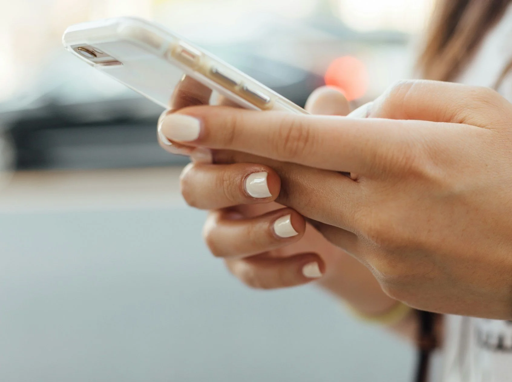 Person holding a smartphone, close-up of hands with white-painted nails.