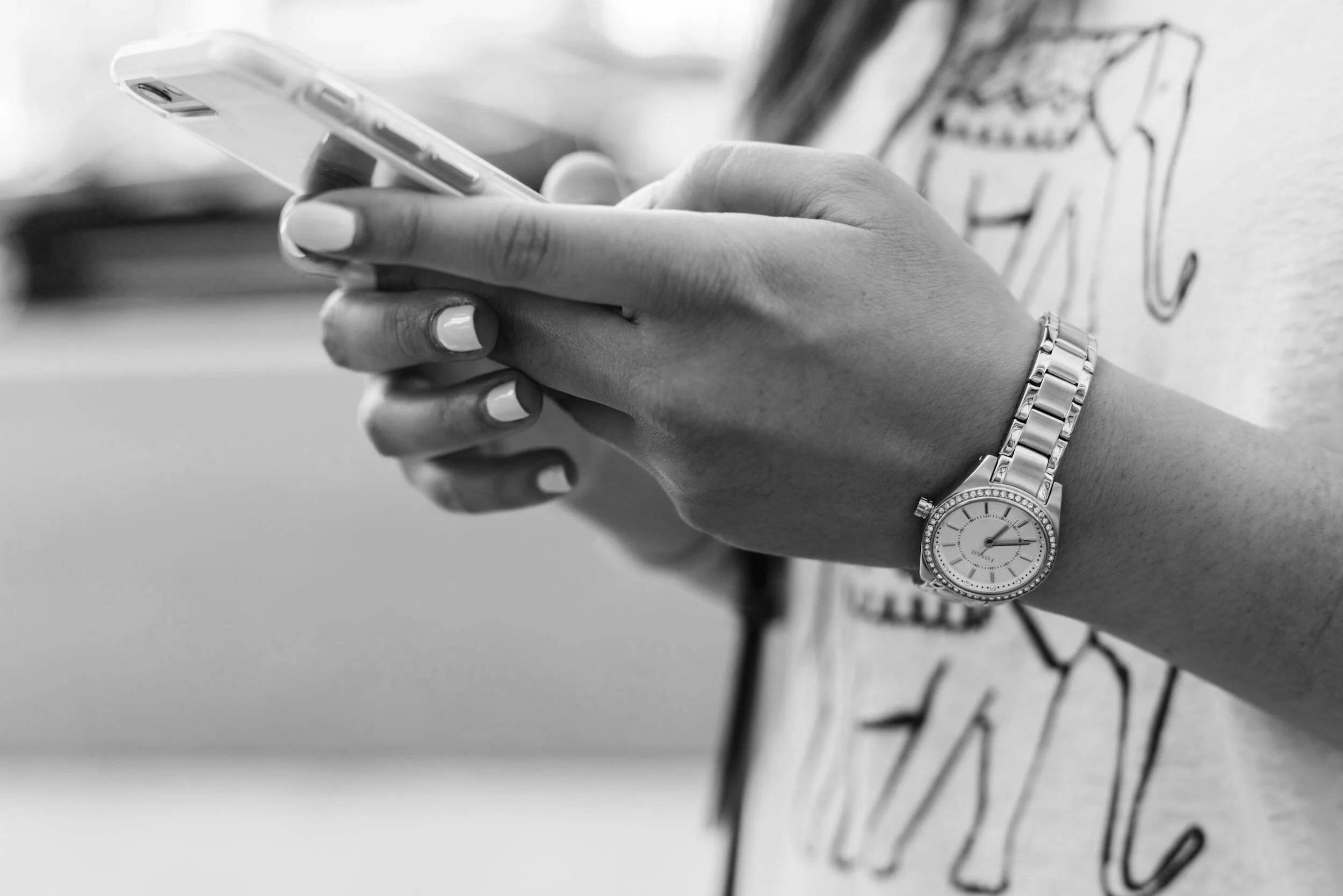 Close-up of a person's hands holding a smartphone, wearing a watch and an elephant print shirt.