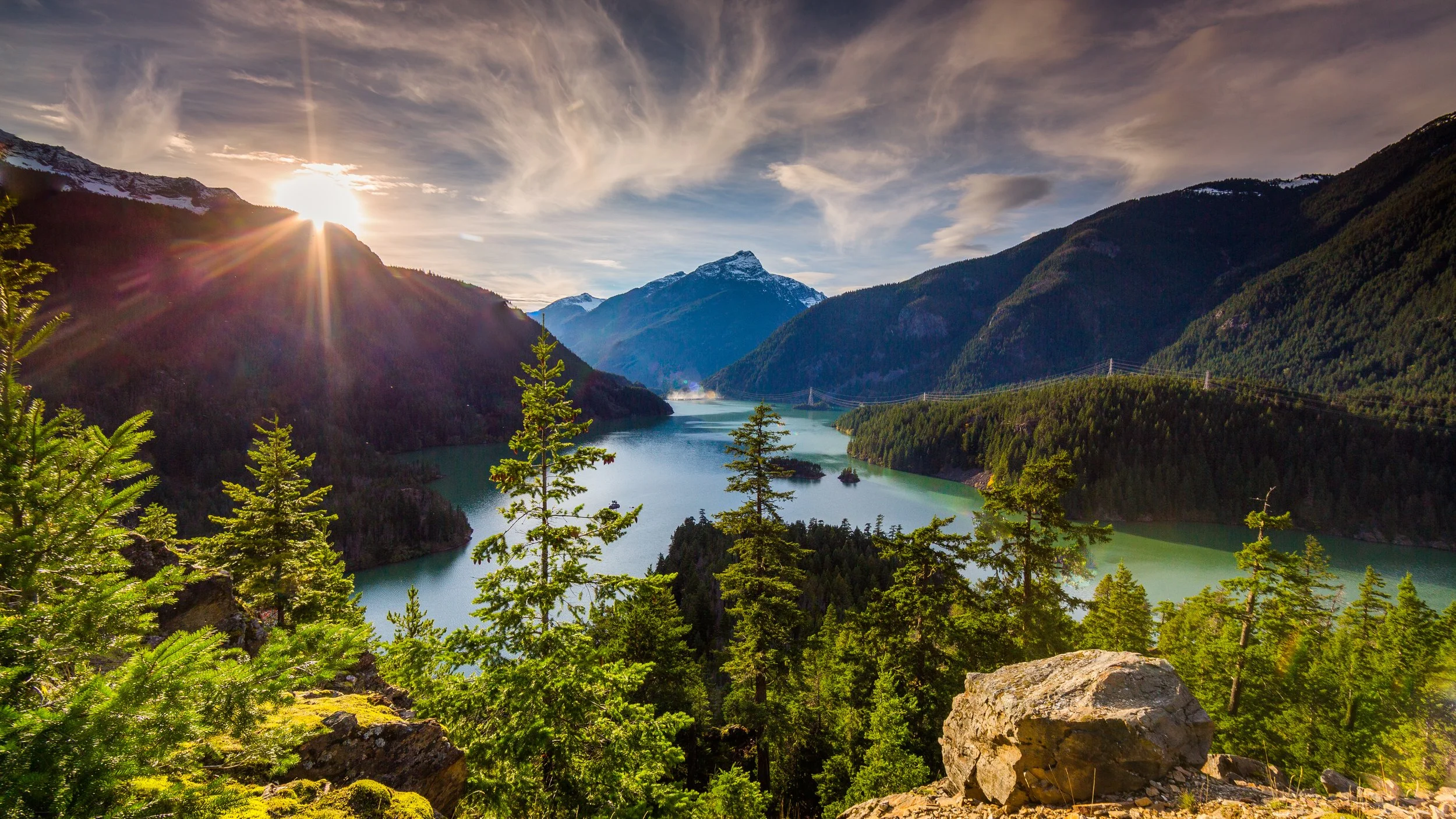 Sunset over a mountain lake surrounded by evergreen forest and snow-capped peaks, representing leadership evolution, discernment, and human capacity.