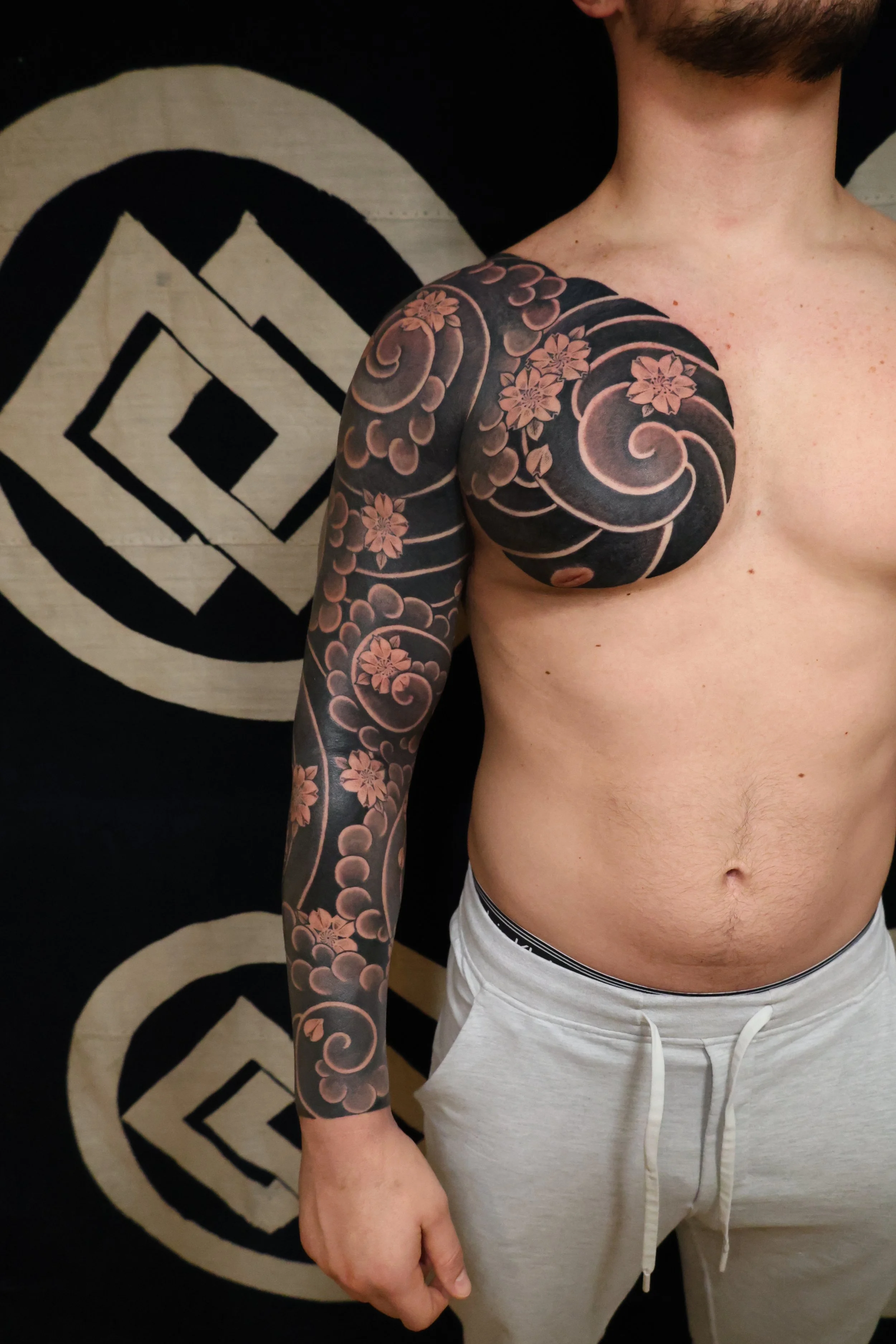 Irezumi blackwork Japanese sleeve with cherry blossoms, wind bar, swirls, and clouds