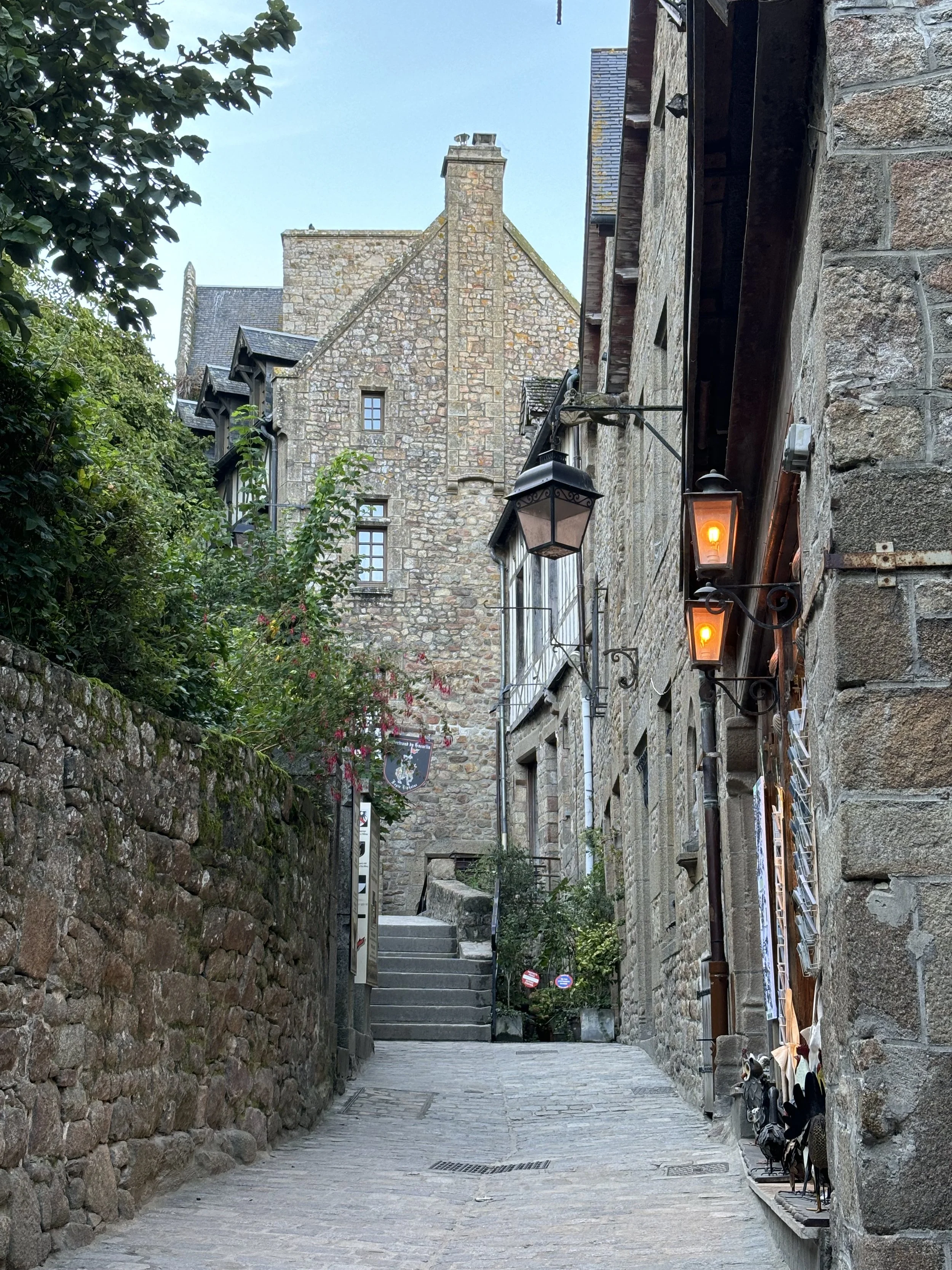 Narrow medieval lane with stone buildings and lanterns inside Mont Saint-Michel, showing the steep streets leading upward through the island.