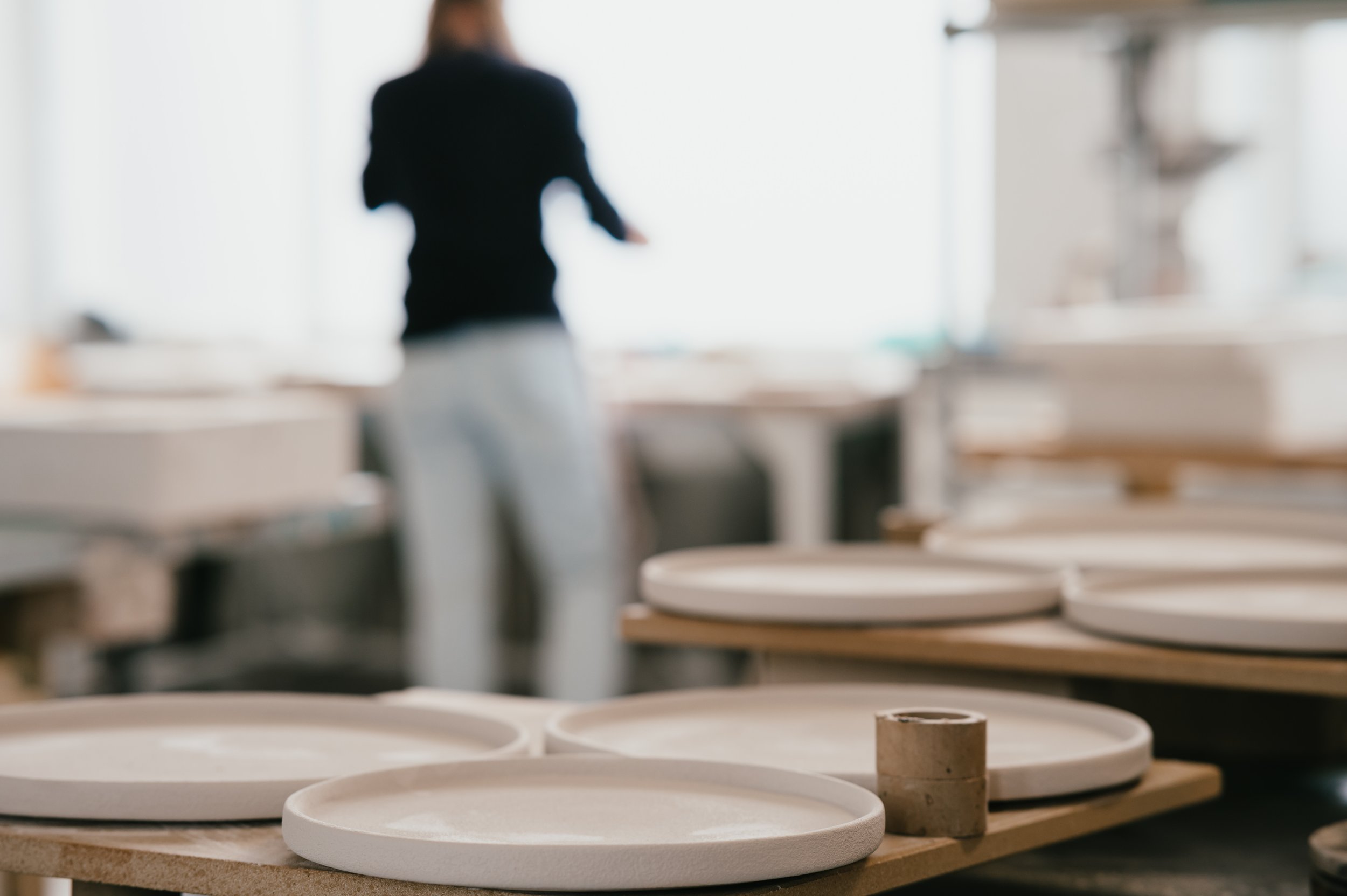 Craft studio with ceramic plates on shelves and a blurred person in the background.