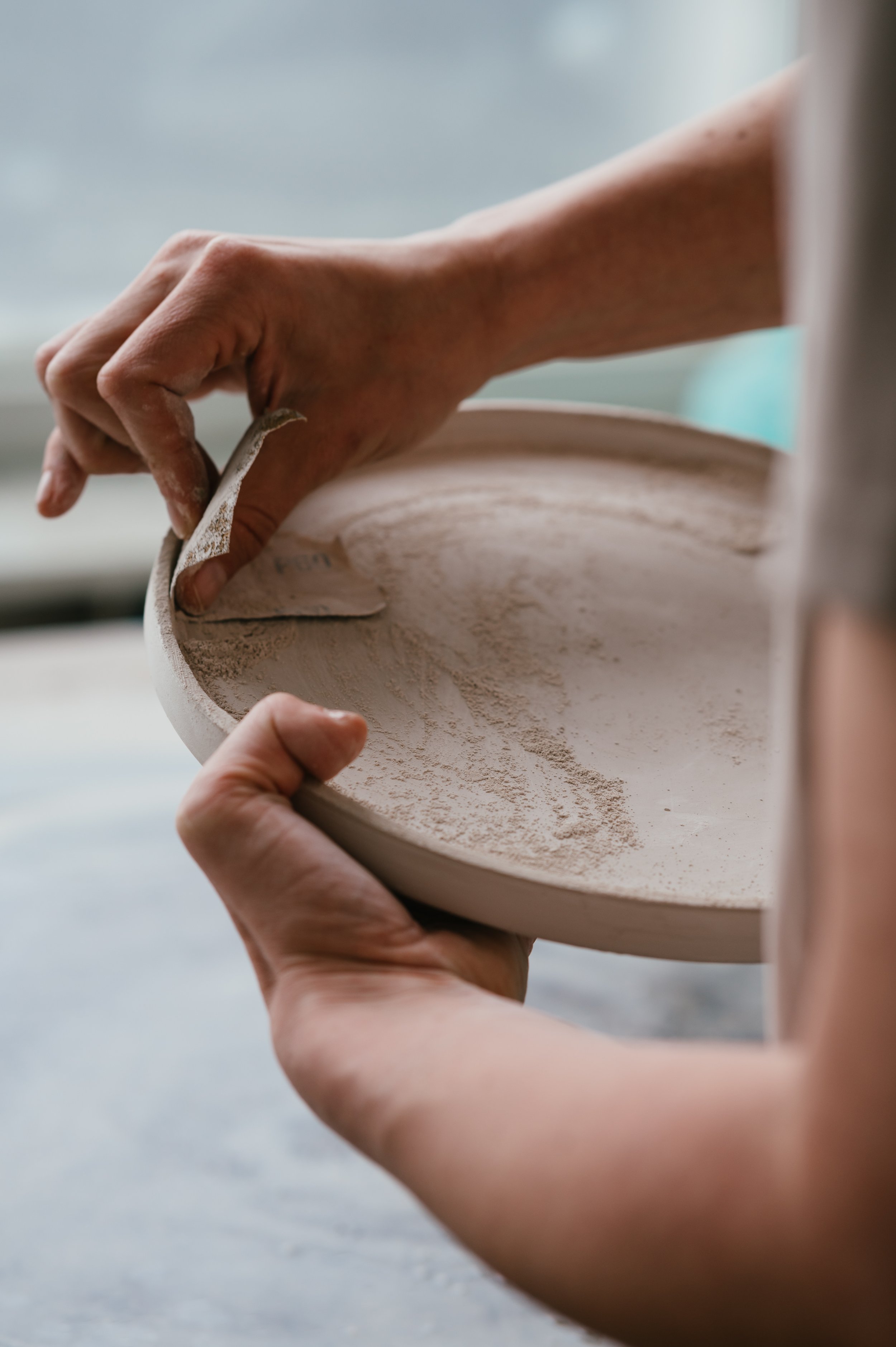 Person sanding a clay plate