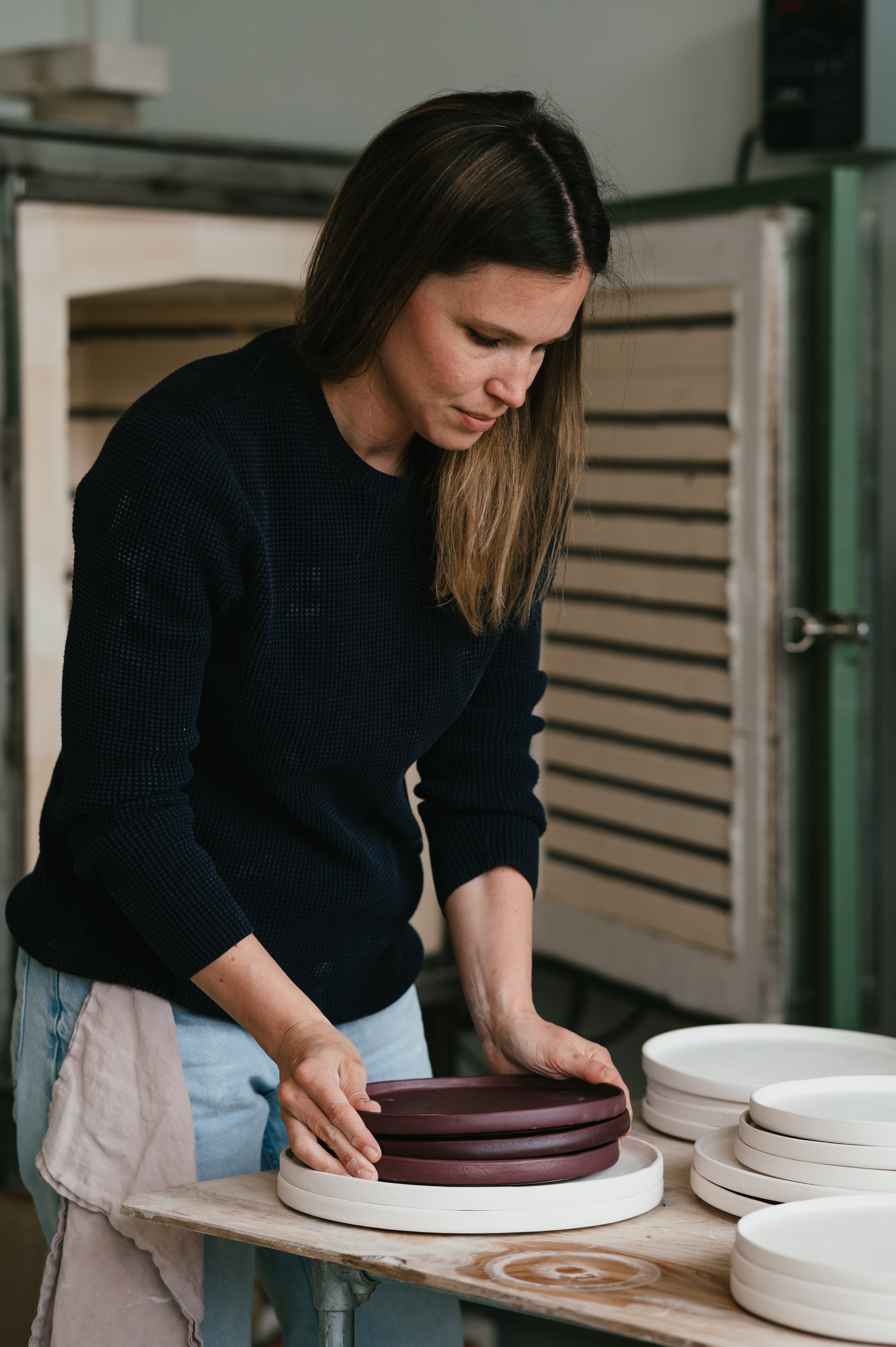 Woman arranging ceramic plates near kiln