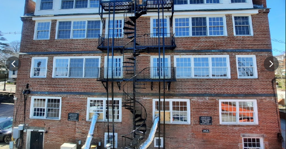 Rear view of a brick apartment building with a black metal fire escape running from the ground to the roof.