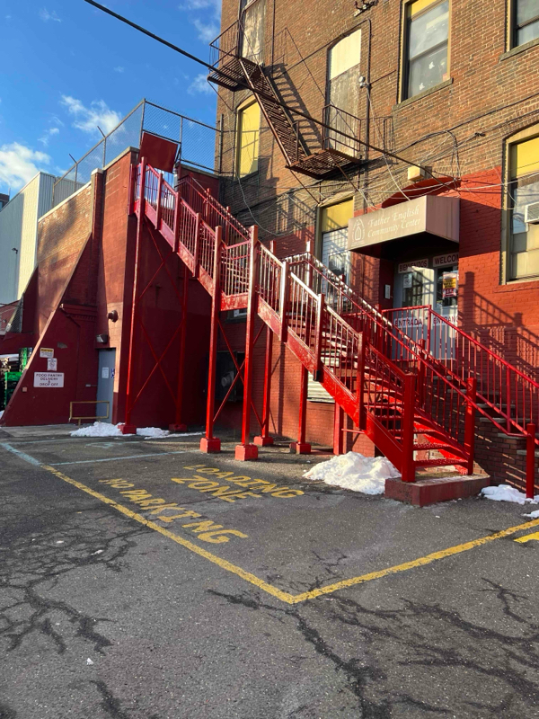 Bright red outdoor stairs and landings stand against a brick building marked for loading and no parking.