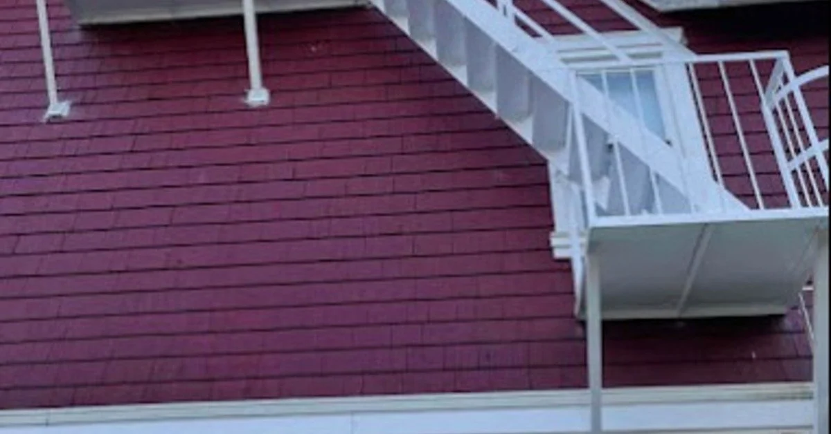 White exterior fire escape runs up a red and cream house, with railings, landings, and a window below.