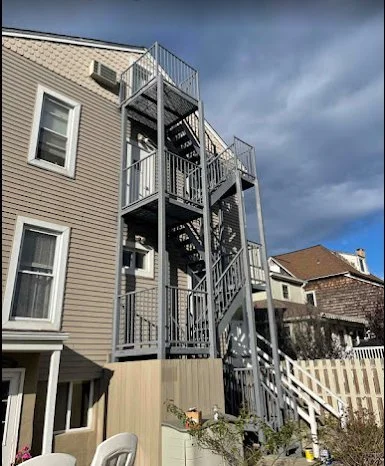 Freestanding metal fire escape with multiple platforms and stair flights beside a house under a dark, cloudy sky.