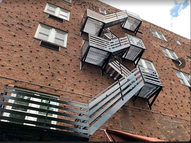 Angled metal fire escape climbs the outside of a brick building, connecting several upper-floor landings.