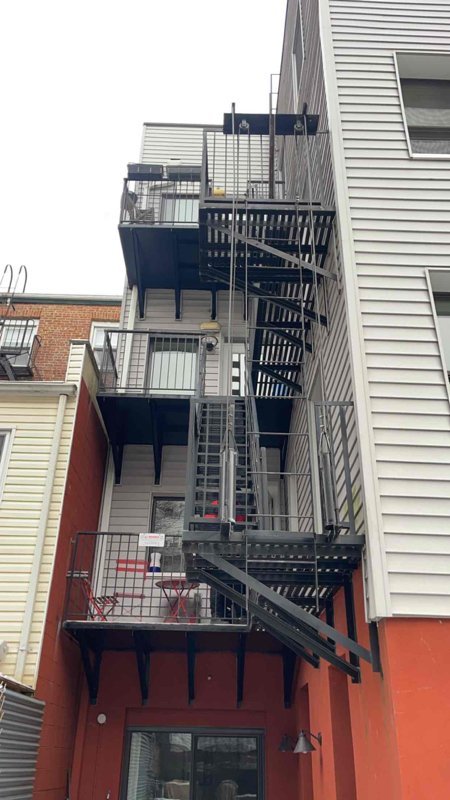 Rear view of a multi-level metal fire escape with balconies, stairs, and safety railings on a townhouse.