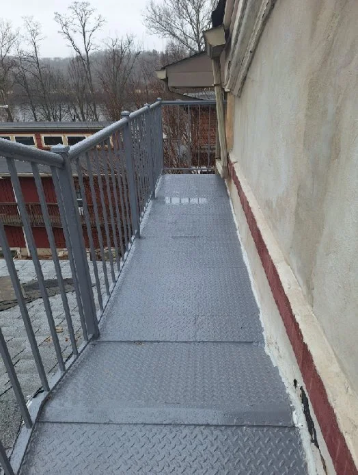 Gray diamond-plate fire escape walkway with metal railings extends along the upper level of a stucco building.