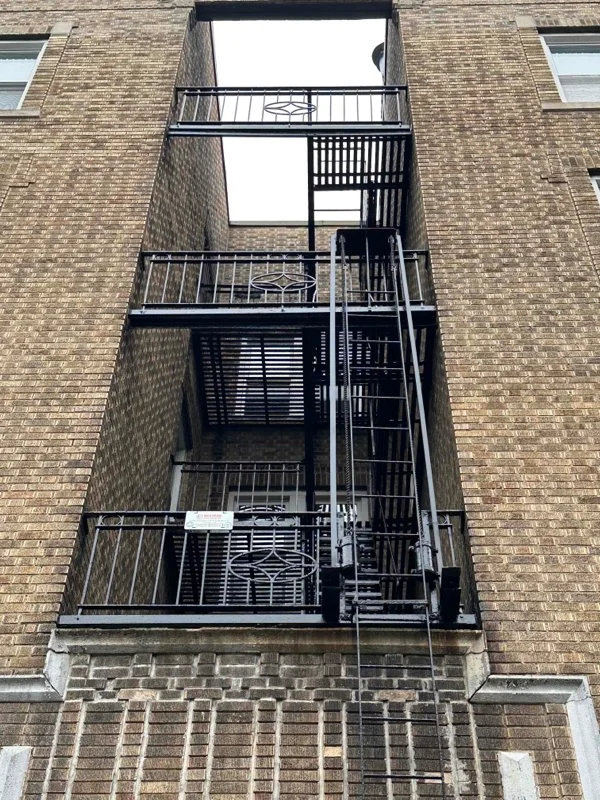 Recessed exterior fire escape features stacked landings, railings, and a vertical ladder between brick walls.